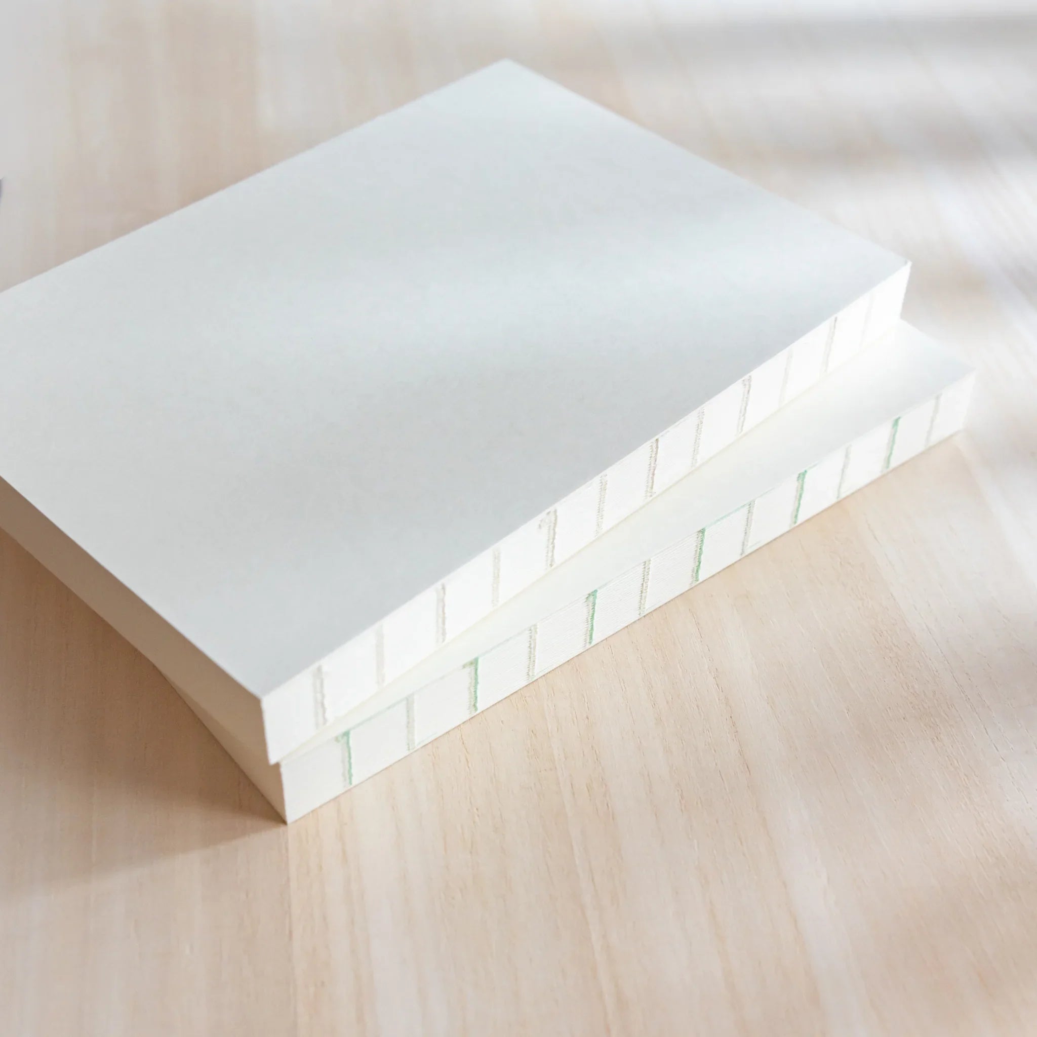 Two stacked Midori MD Notebooks shown spine-side, exposed cross-stitch thread binding in green and beige