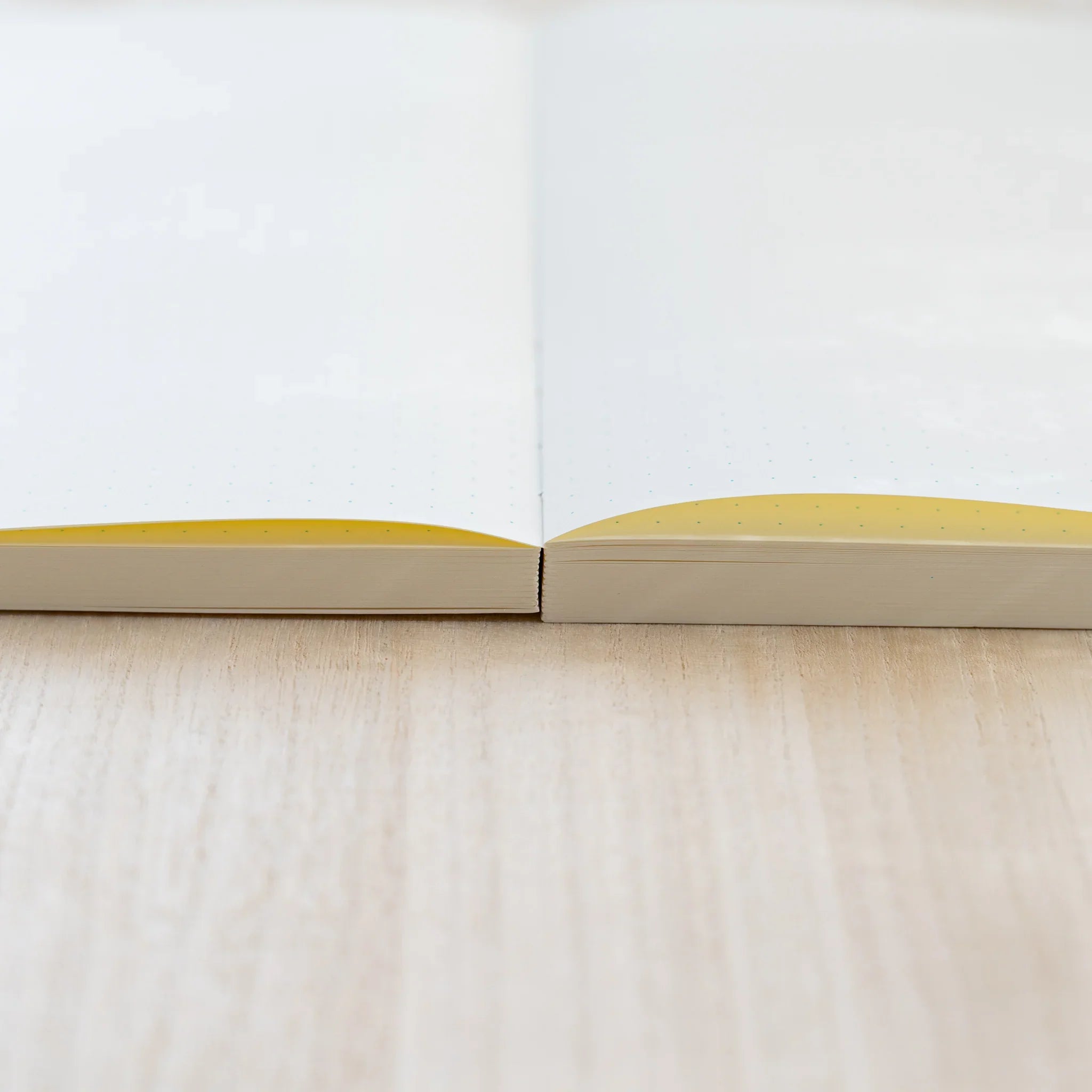 Low-angle view of a Midori MD Notebook Journal lying open and flat on wood, showing cream dot grid pages