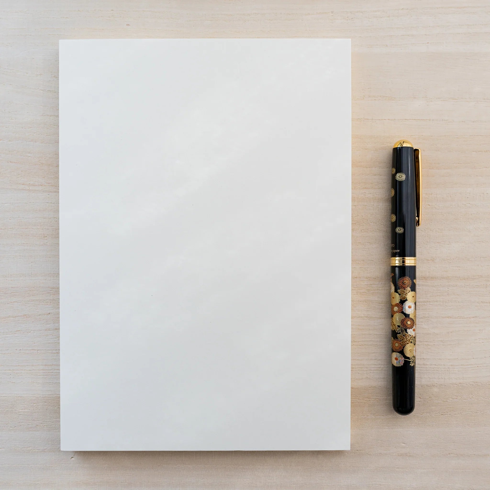 Midori MD Notebook Thick plain blank cream cover with a black gold-floral Japanese fountain pen alongside, on light wood