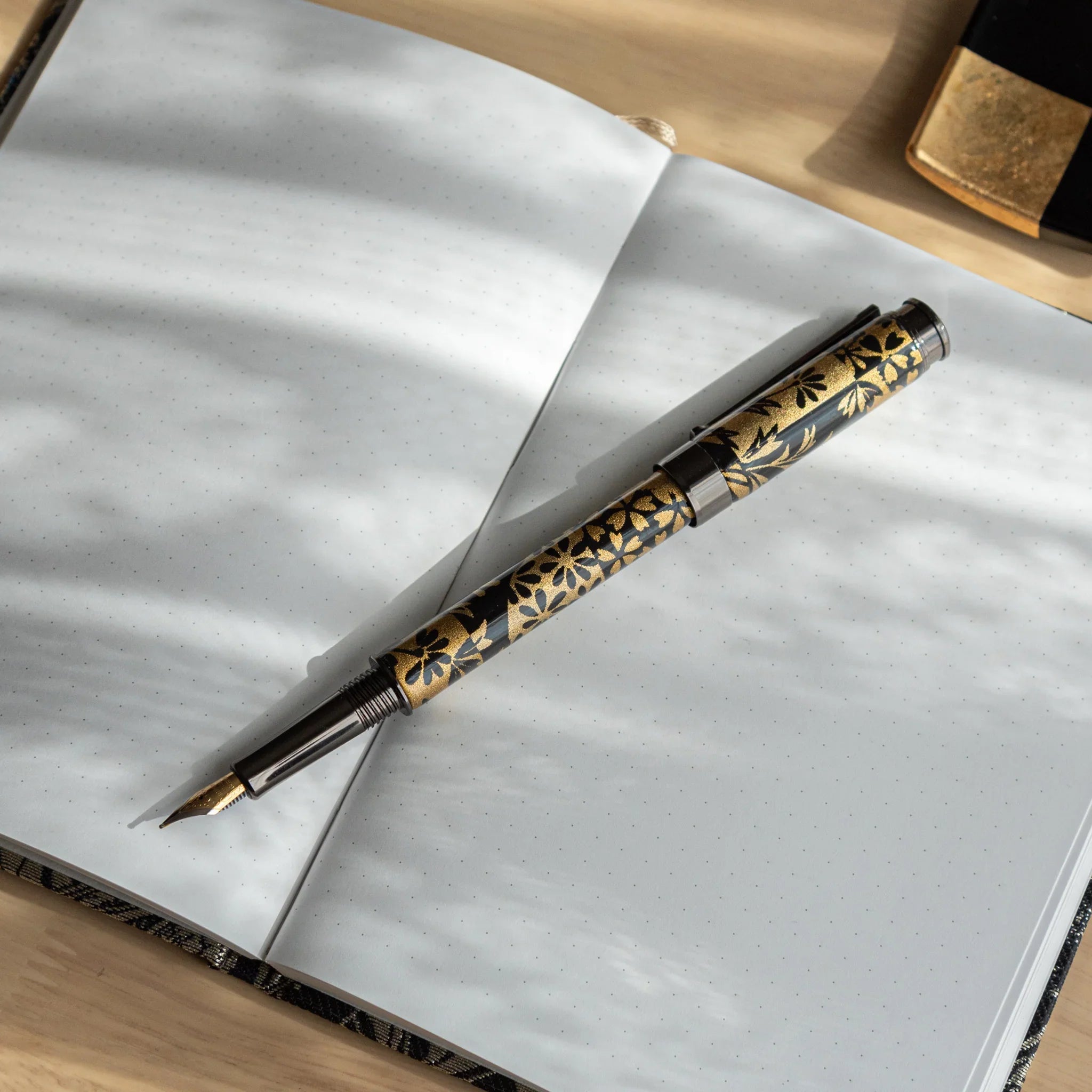 Dark fountain pen with black and gold autumn botanical pattern wrapper positioned on light wooden surface angle