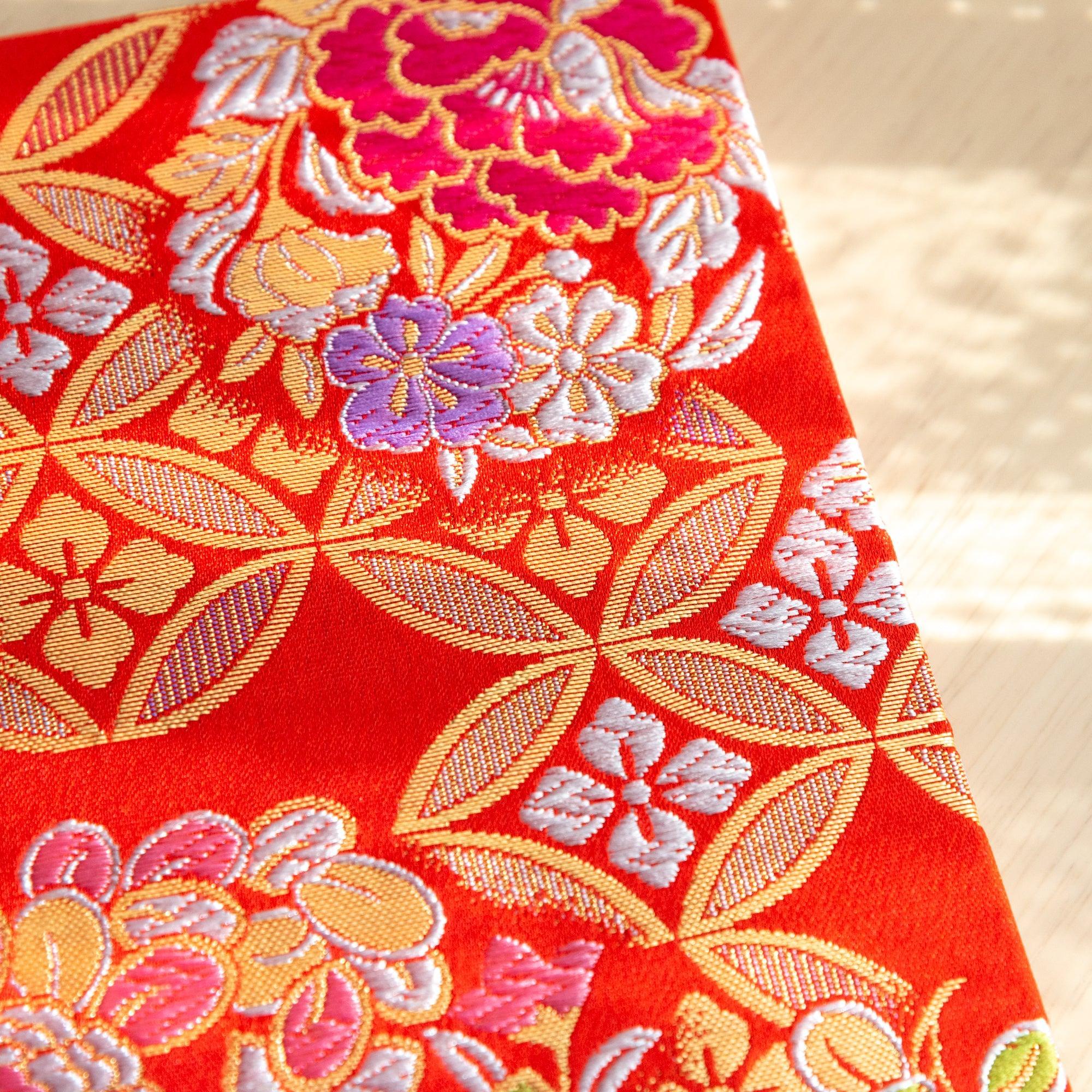 Top edge view of Nishijin textile notebook showing orange-red woven cover with gold shippo lattice and colorful floral motifs