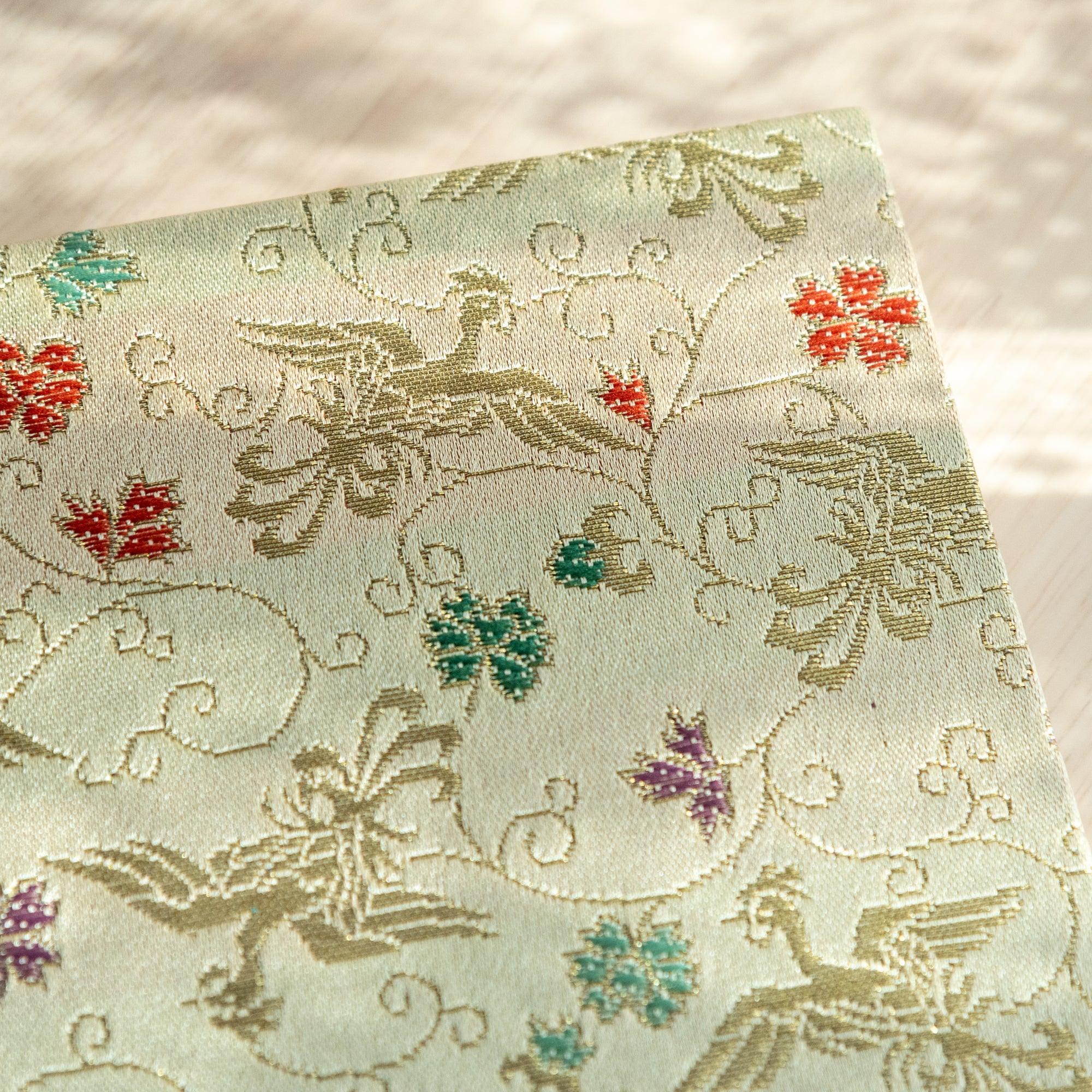 Corner close-up of Nishijin woven textile notebook in cream gold with phoenix birds and colorful flowers in red and teal