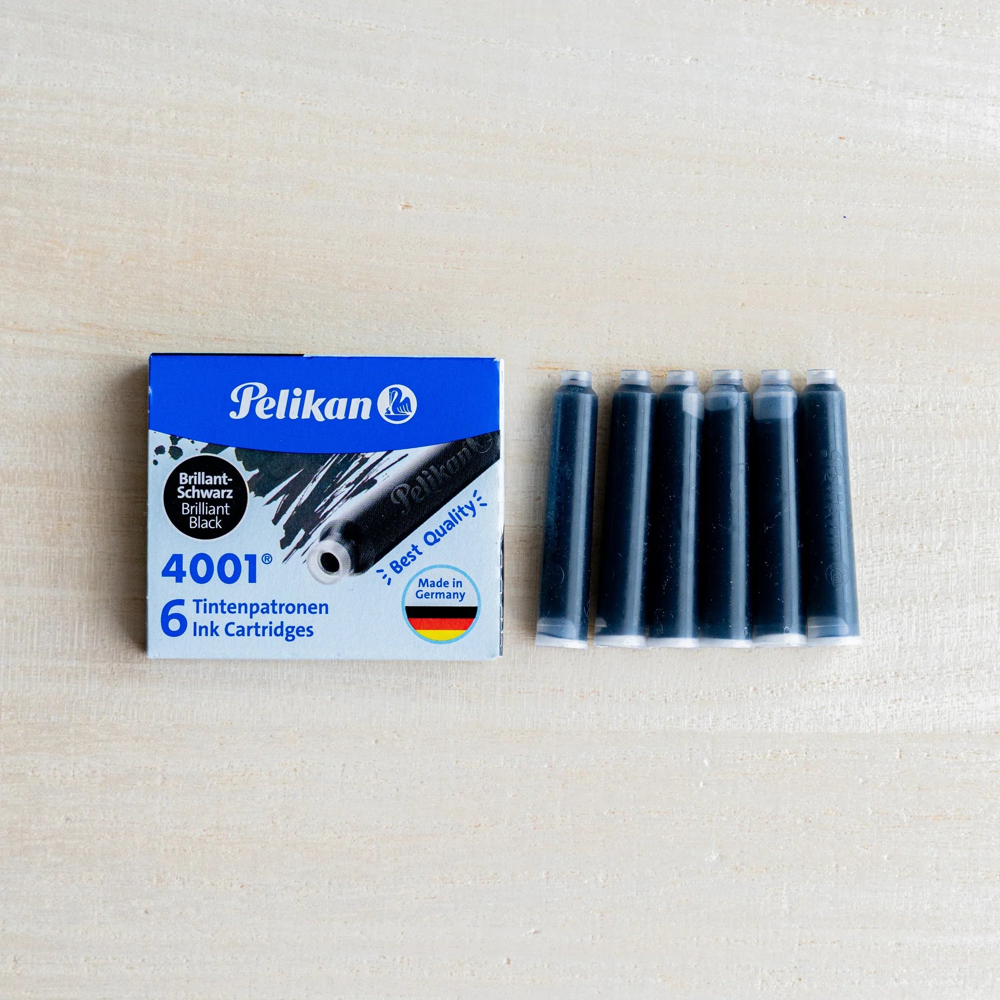 Pelikan 4001 black ink cartridge box beside six black fountain pen ink cartridges in a row, on light wood