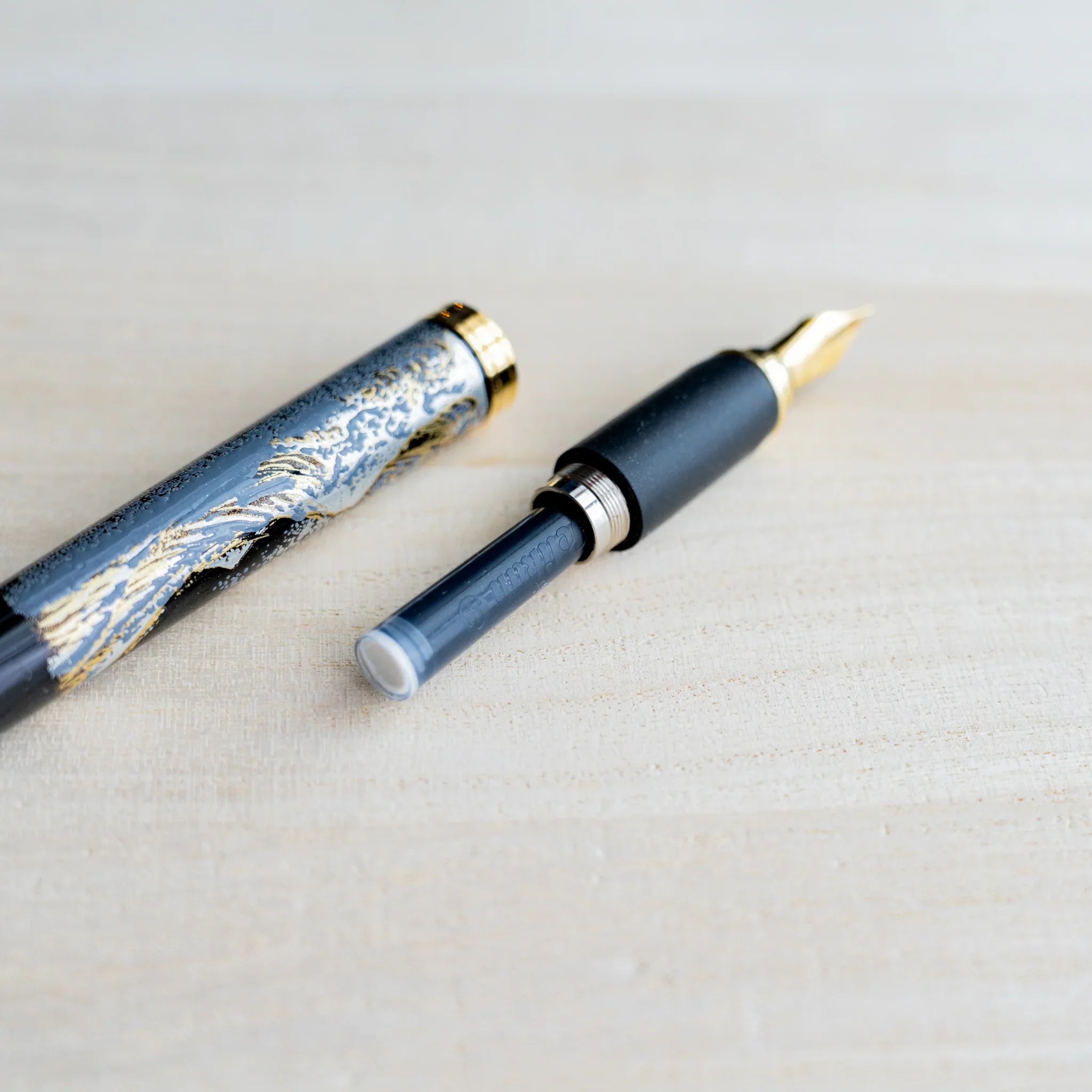 Black Yamanaka fountain pen taken apart with gold nib section and a Pelikan ink cartridge attached, barrel and cap beside