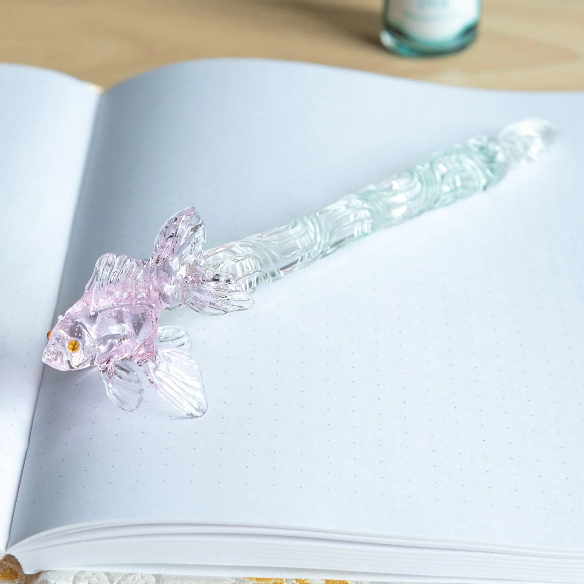 Pink glass dip pen with goldfish motif captured from angled view showing translucent barrel and metal nib shine