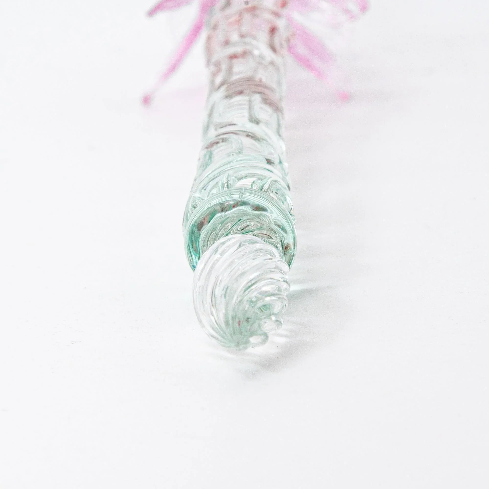 Pink glass pen with twisted metal nib displayed to showcase ornate handle and pale pink translucent barrel shine