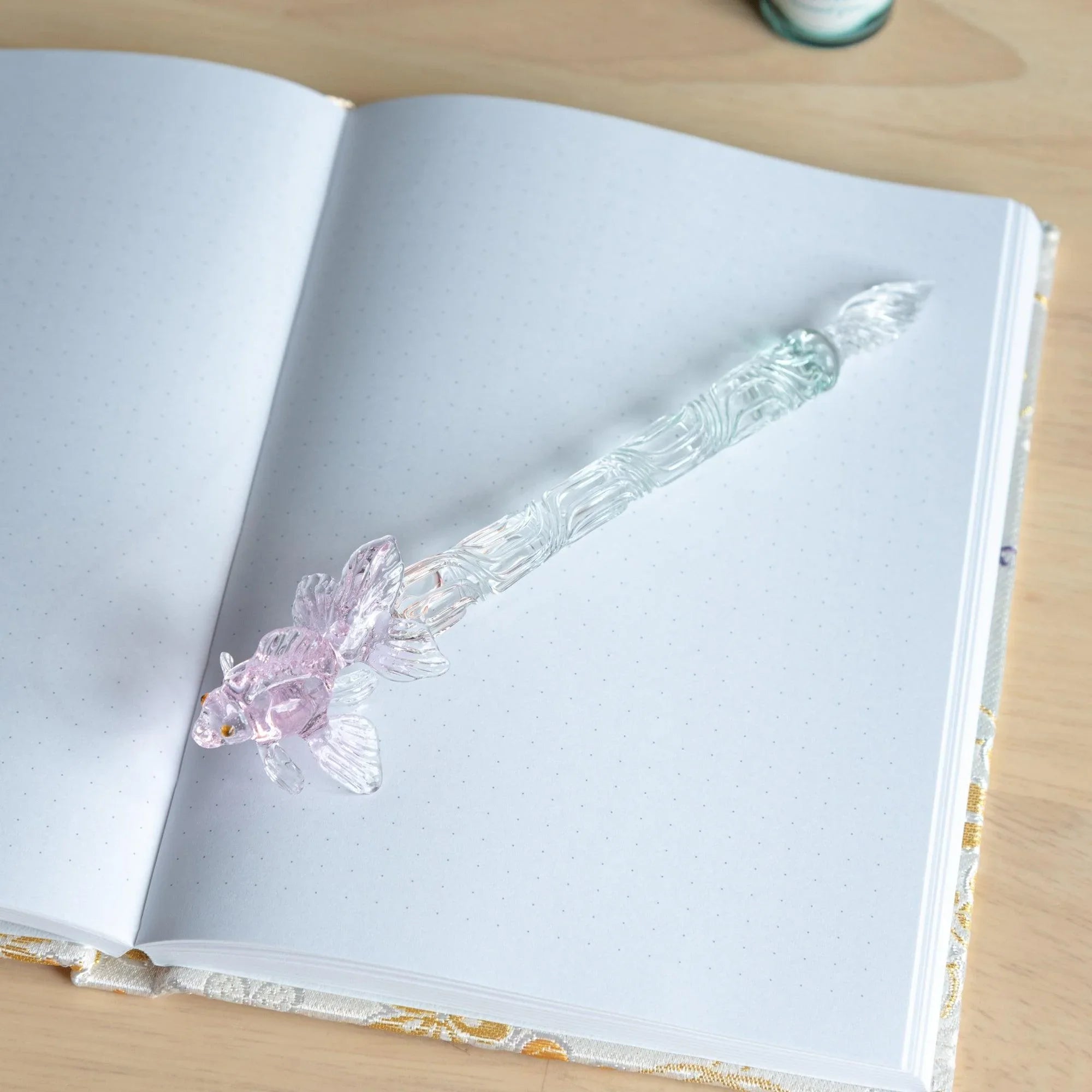 Goldfish-themed pink glass dip pen shown at angle with twisted metal nib and translucent barrel detail with holder
