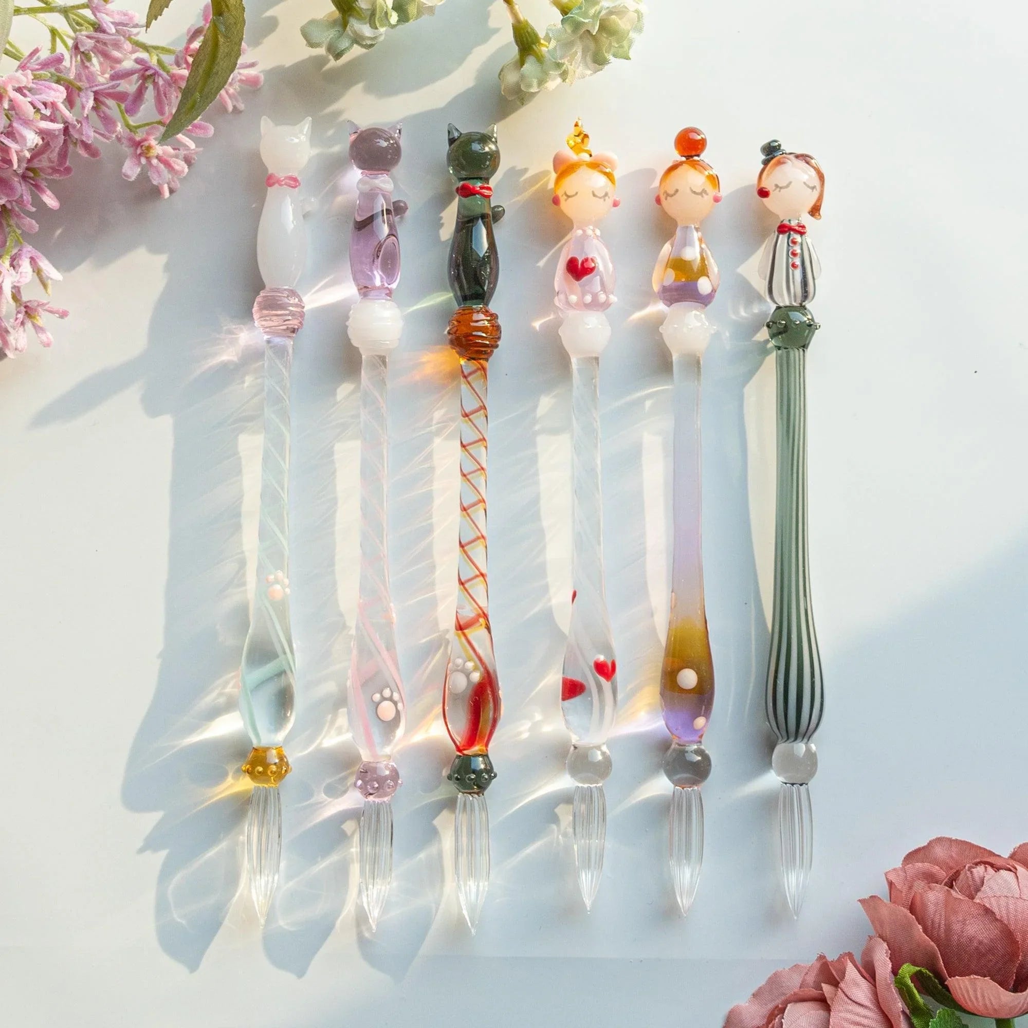 Pink sitting Nyanko cat figurine with spiral-patterned glass dip pen handle in close-up detail photography