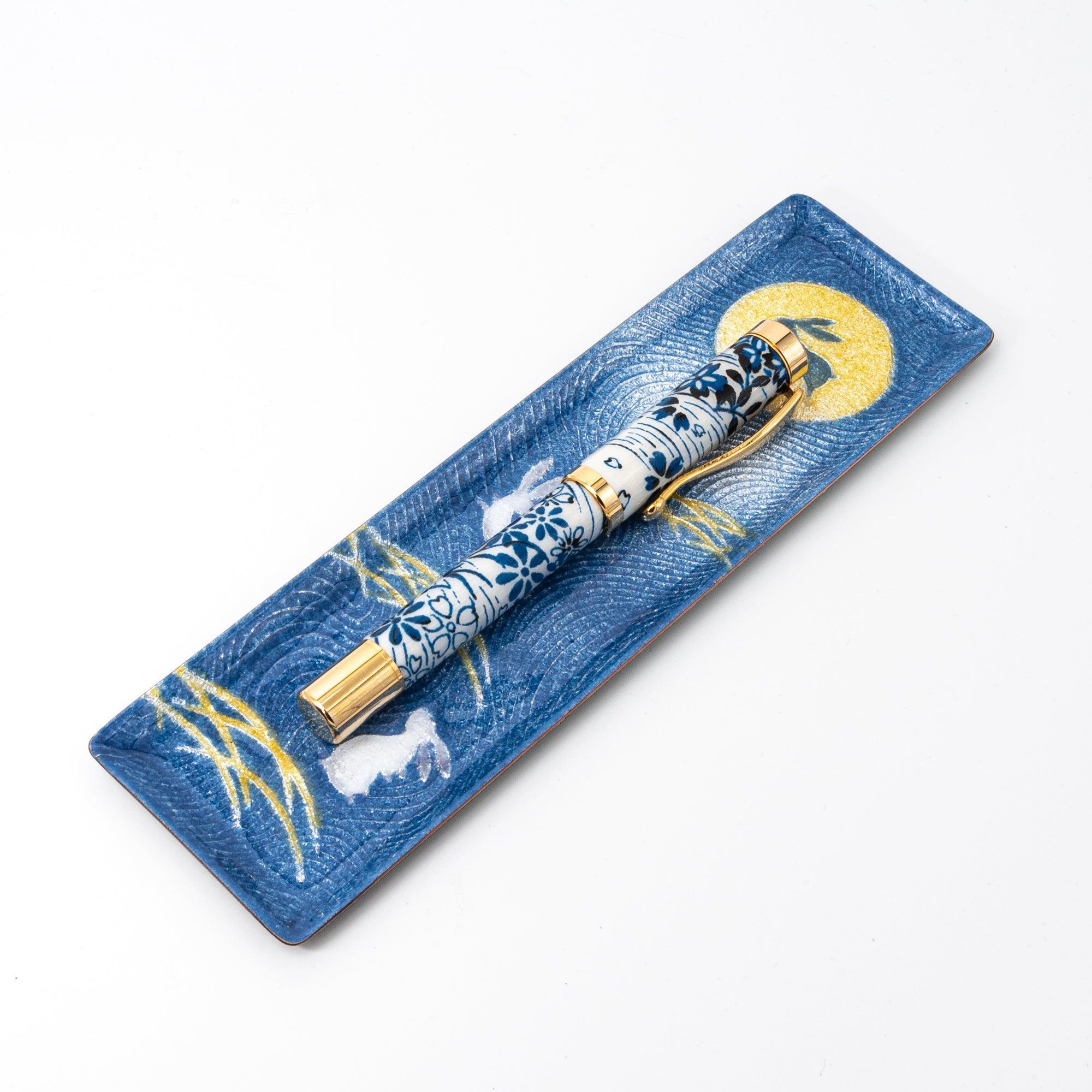 Dark blue enamel slim pen tray with rabbit and moon design, angled view on white background, blue floral pen resting on tray