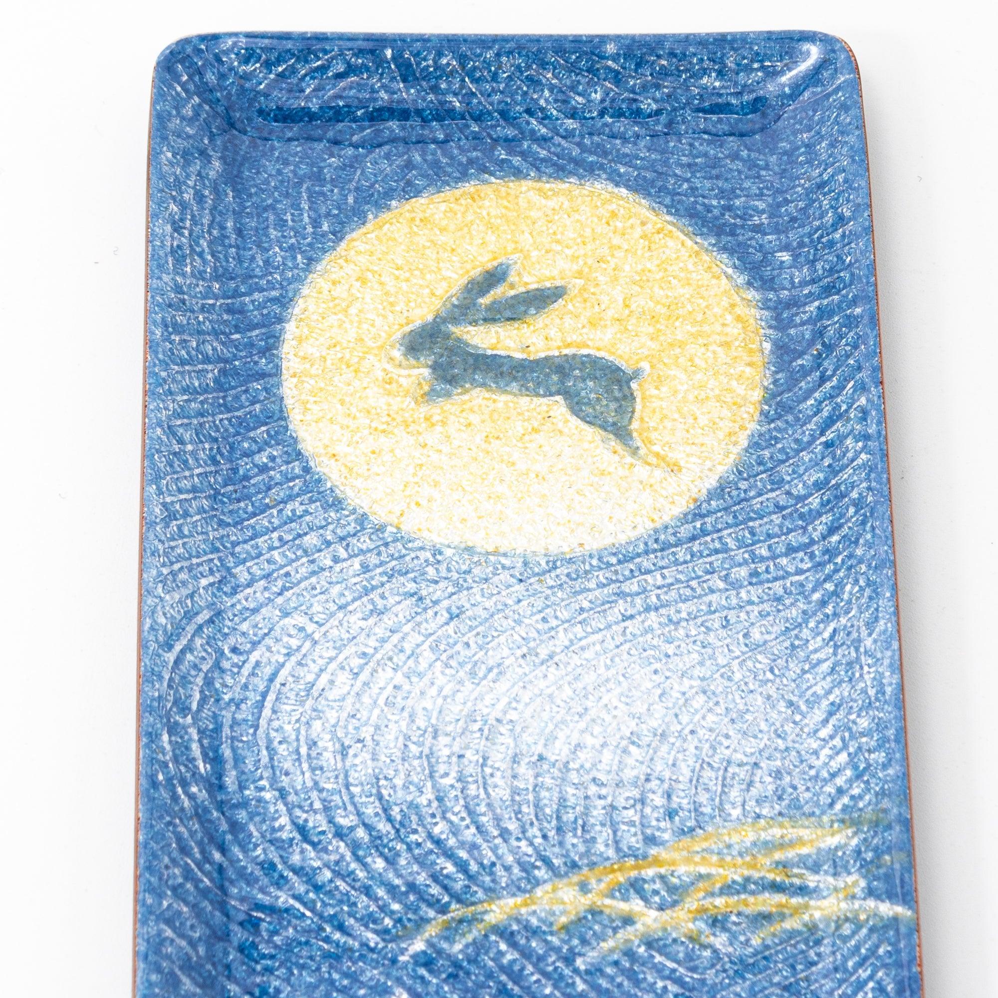 Close-up of dark blue enamel tray showing gold full moon with leaping rabbit silhouette and wave pattern on blue enamel