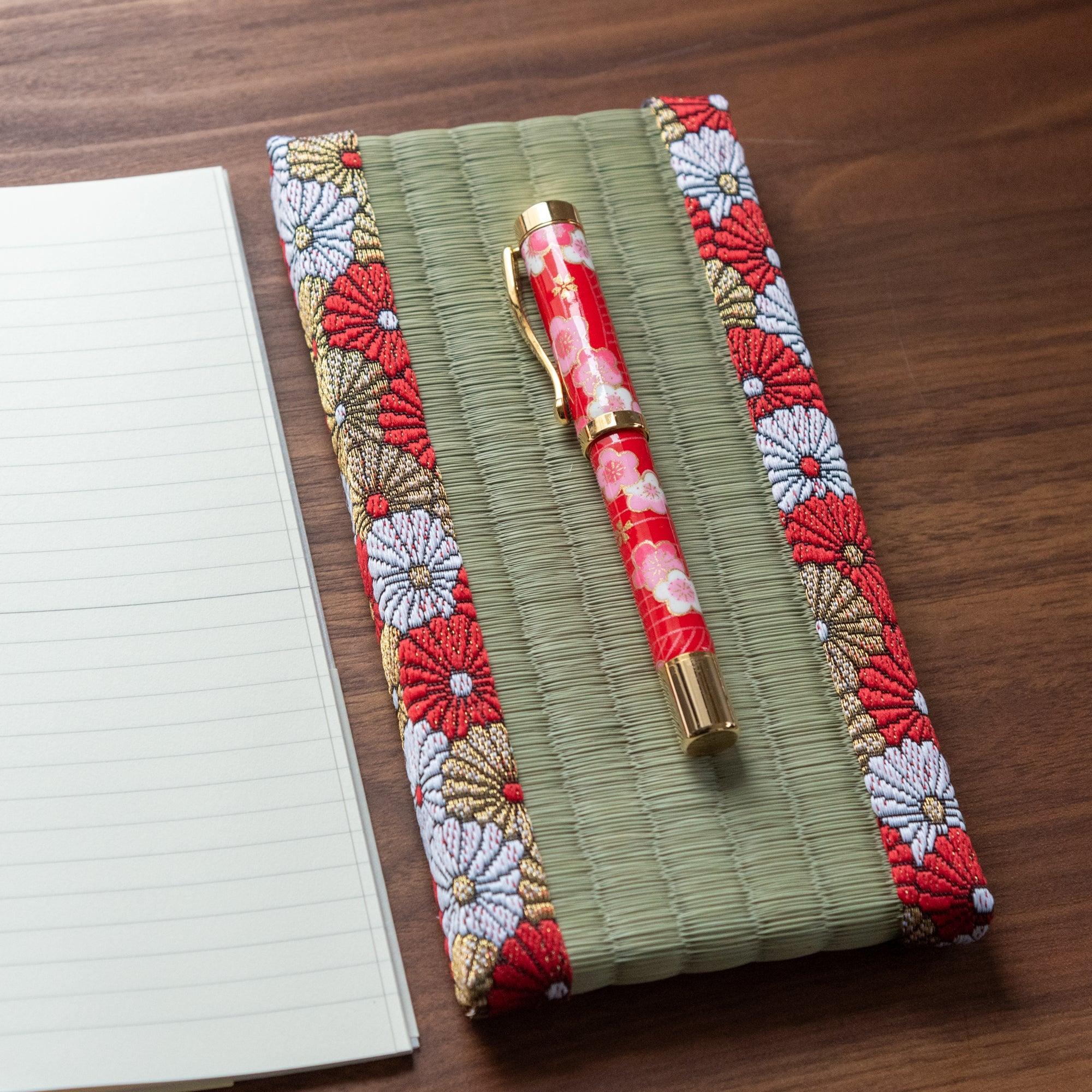 Japanese tatami pen tray with chrysanthemum brocade border holding a red floral fountain pen, angled view with ruled notebook