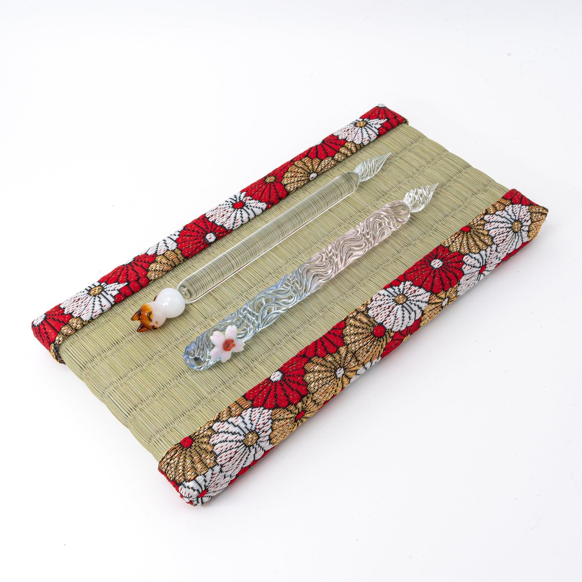 Japanese tatami pen tray with chrysanthemum brocade border holding two glass dip pens on white background, angled view