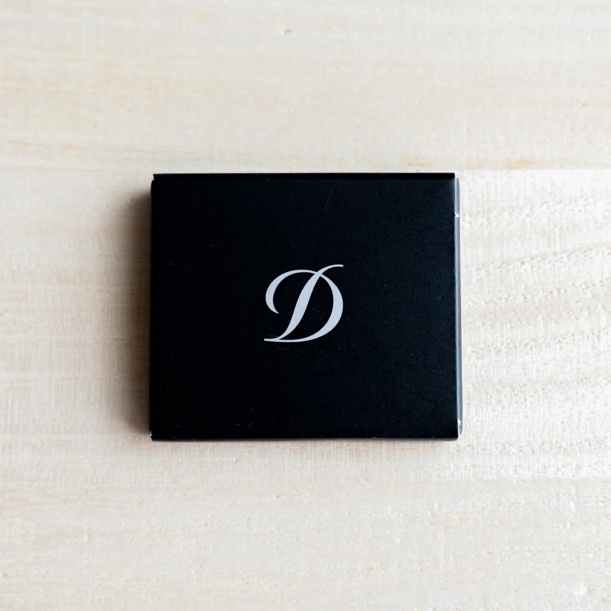 Closed black S.T. Dupont ink cartridge box with white cursive D logo on top, on light wood