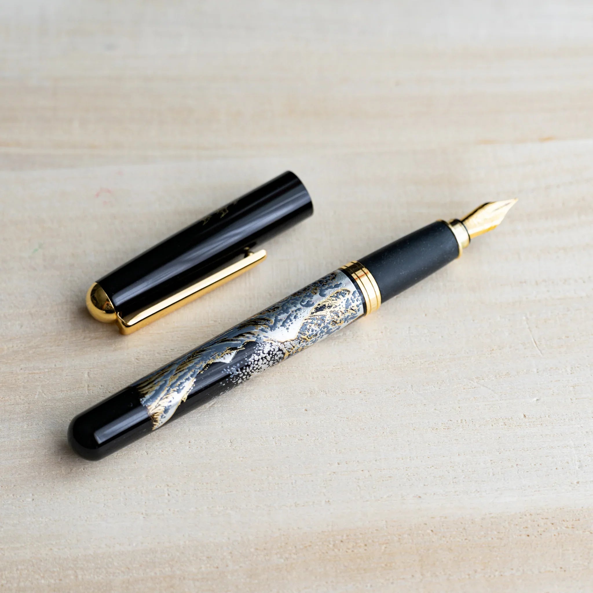 Black Yamanaka fountain pen uncapped with gold and silver landscape urushi design, gold nib and trim, cap beside it