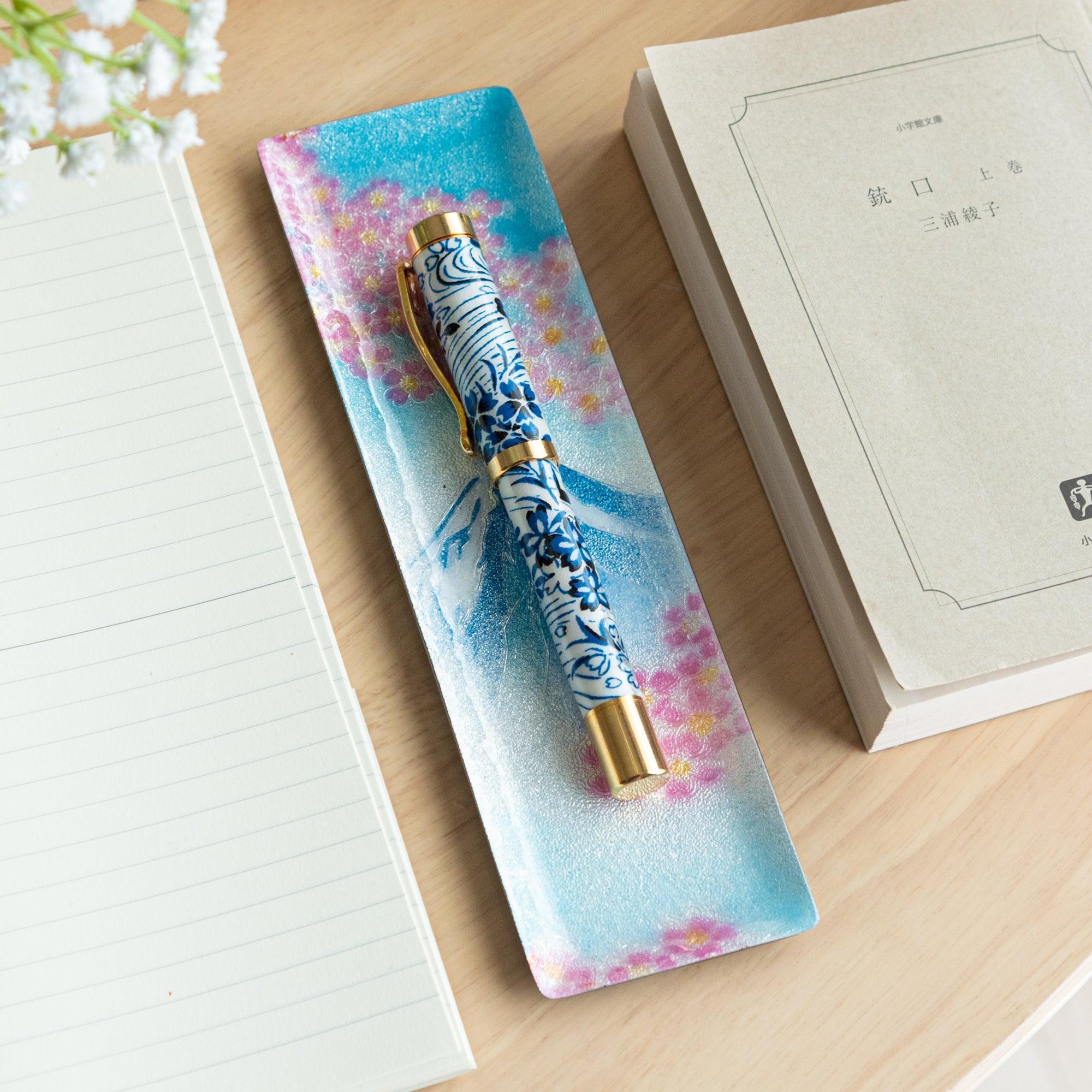Japanese shippo ware slim pen tray with Mt. Fuji and sakura on blue enamel, holding a blue floral fountain pen on a wood desk