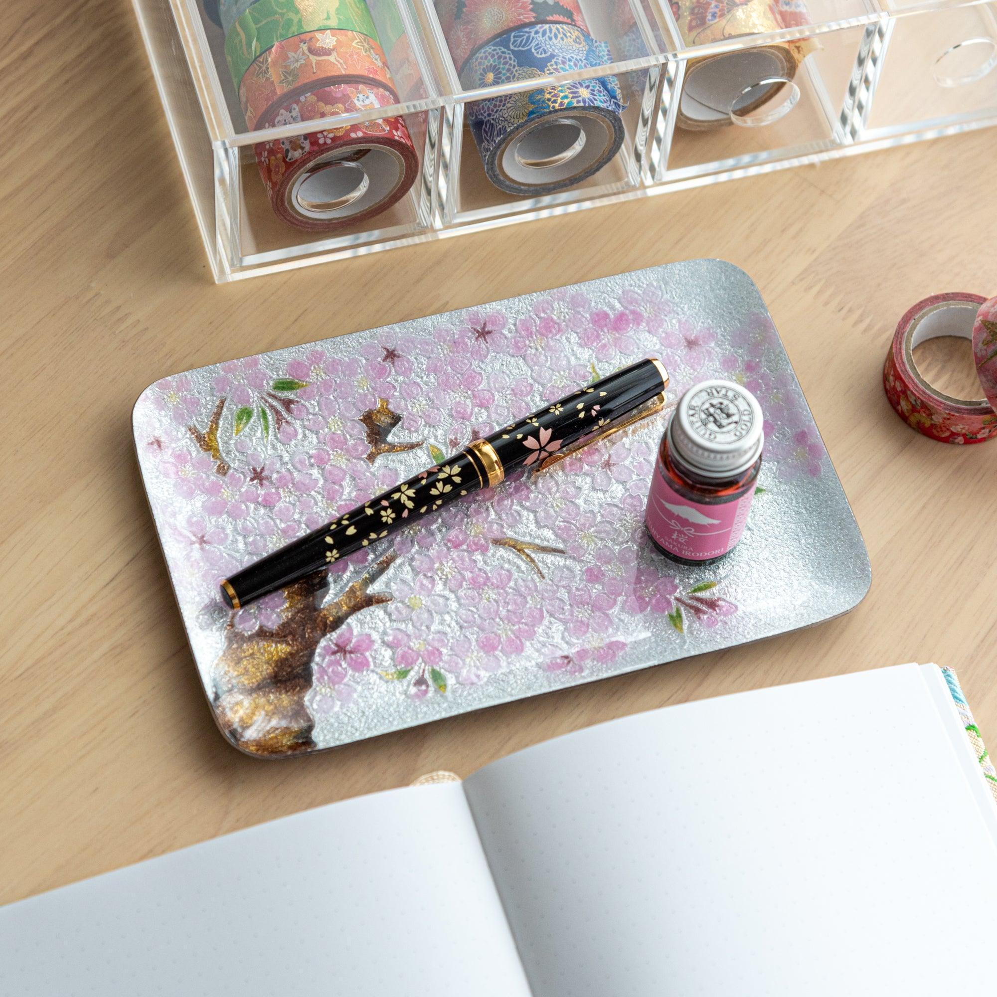 Sakura shippo ware silver pen tray with pink blossom design, holding a black fountain pen and ink bottle on a wood desk