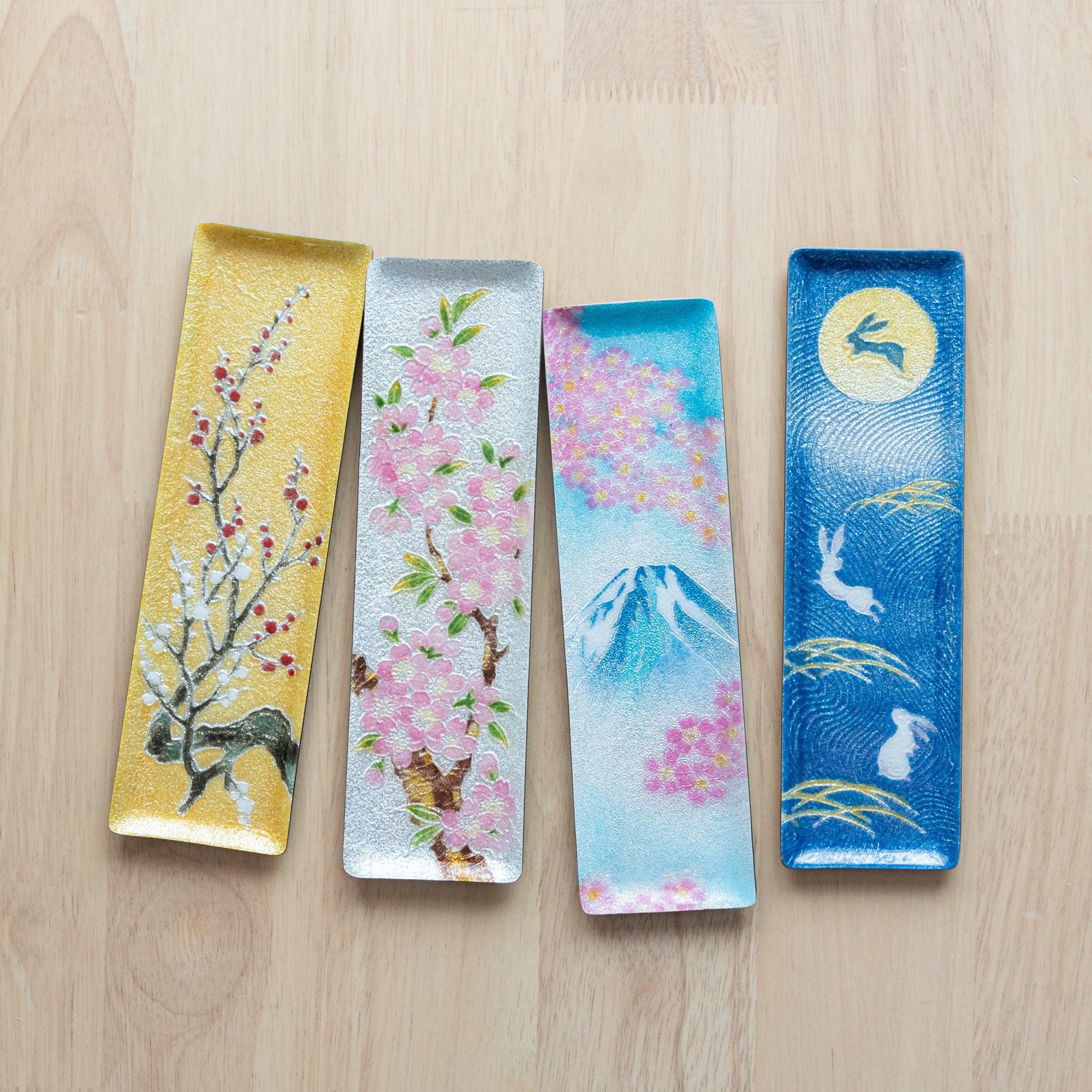 Four Japanese shippo ware slim pen trays on wood: gold plum, silver sakura, blue Fuji with sakura, and dark blue moon rabbit