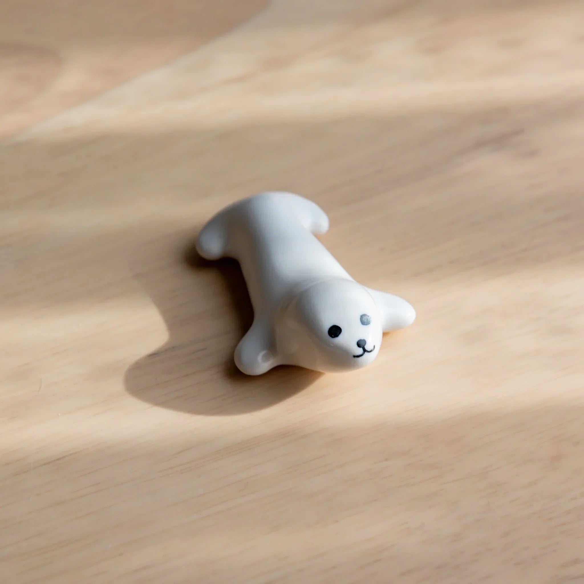 White ceramic seal-shaped Japanese pen rest lying on belly on wood surface, with black dot eyes and painted smile