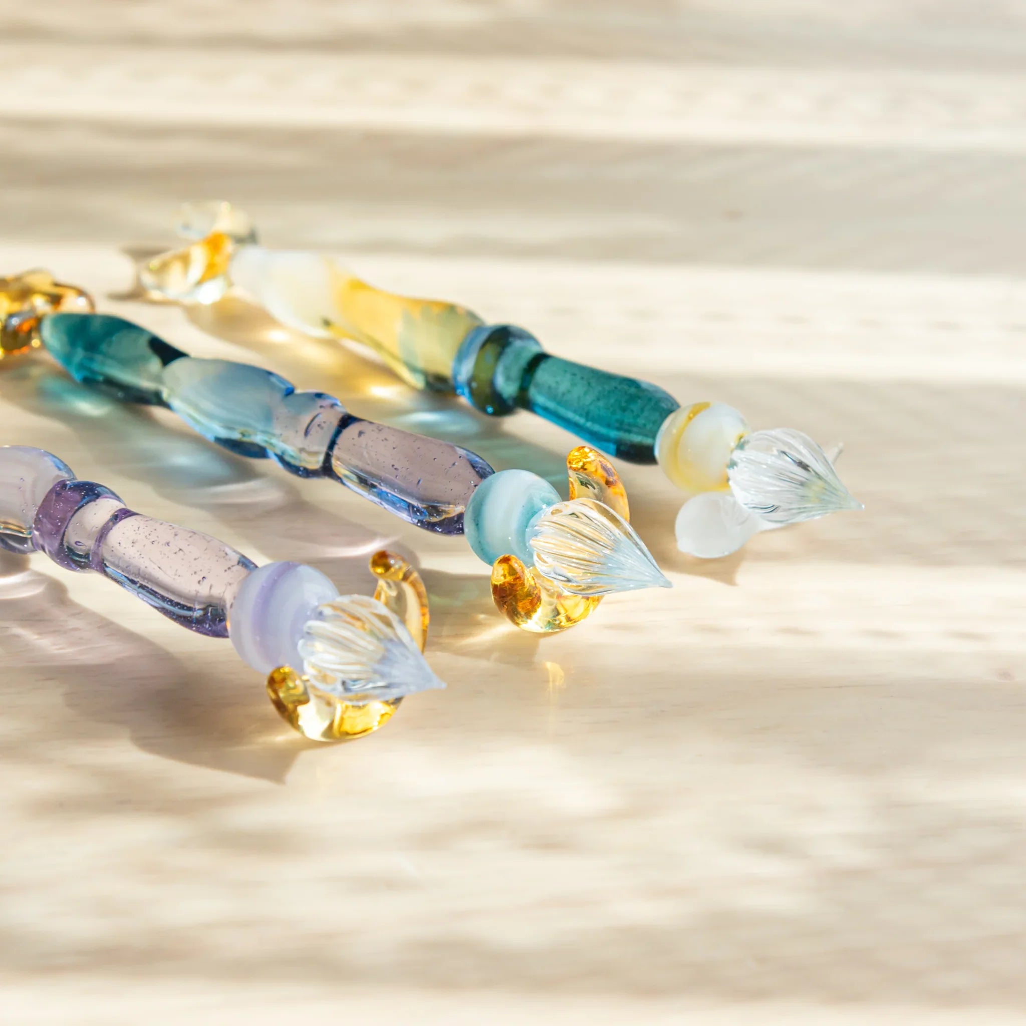 Starlit Night glass dip pens with decorative star-shaped pen rests in purple, teal and cream arranged in row on wood
