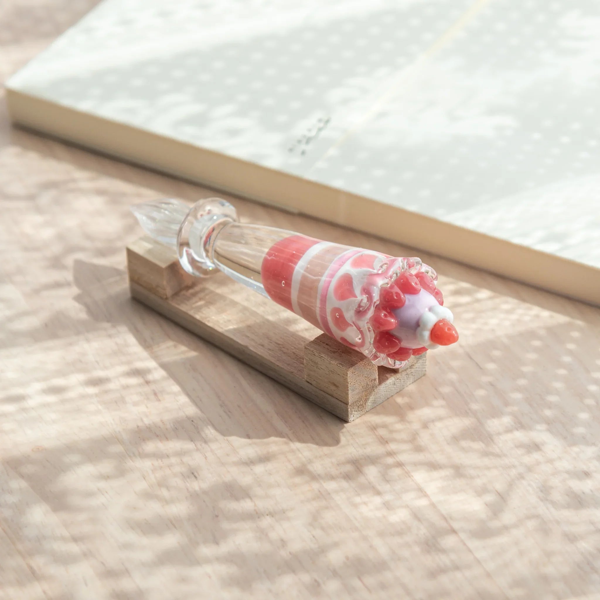 Japanese glass dip pen with strawberry parfait grip on natural wood pen rest, showing lavender dome and red cherry tip detail