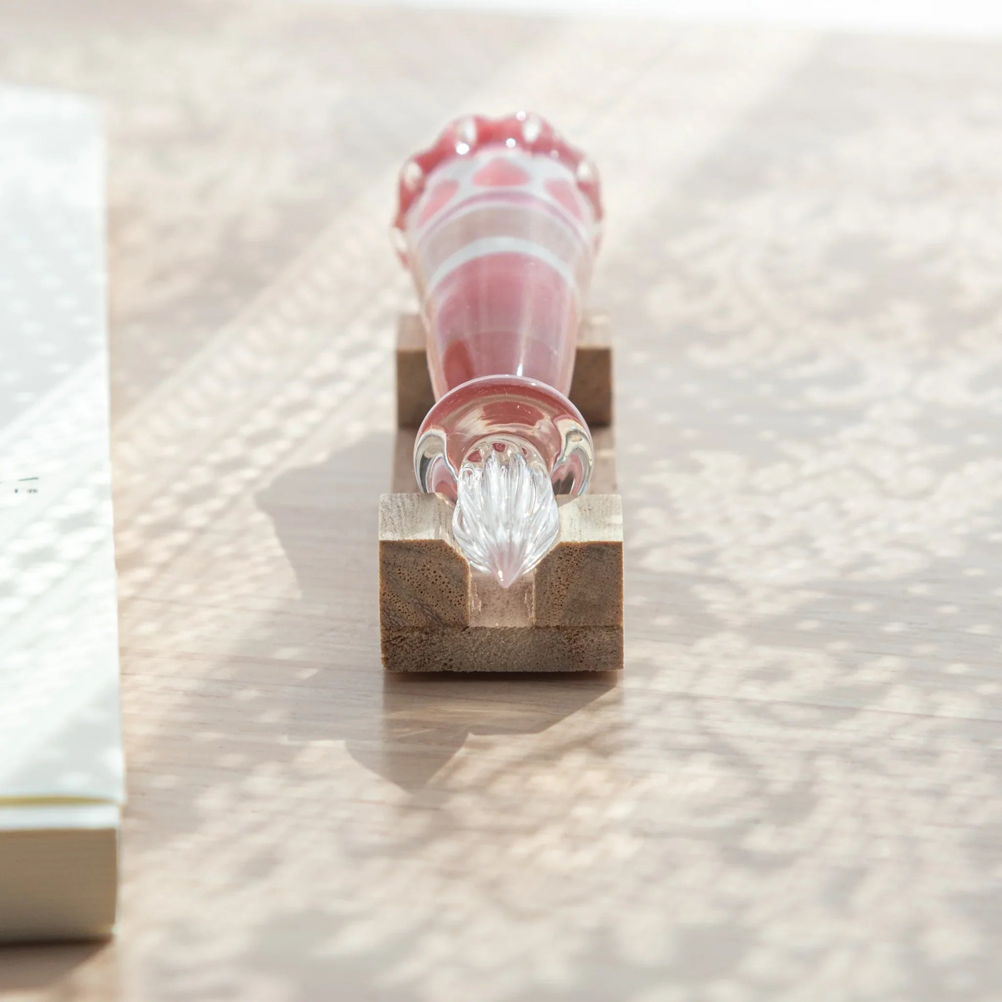 Top-down view of Japanese glass dip pen on wood pen rest showing spiral glass nib below and strawberry parfait grip above