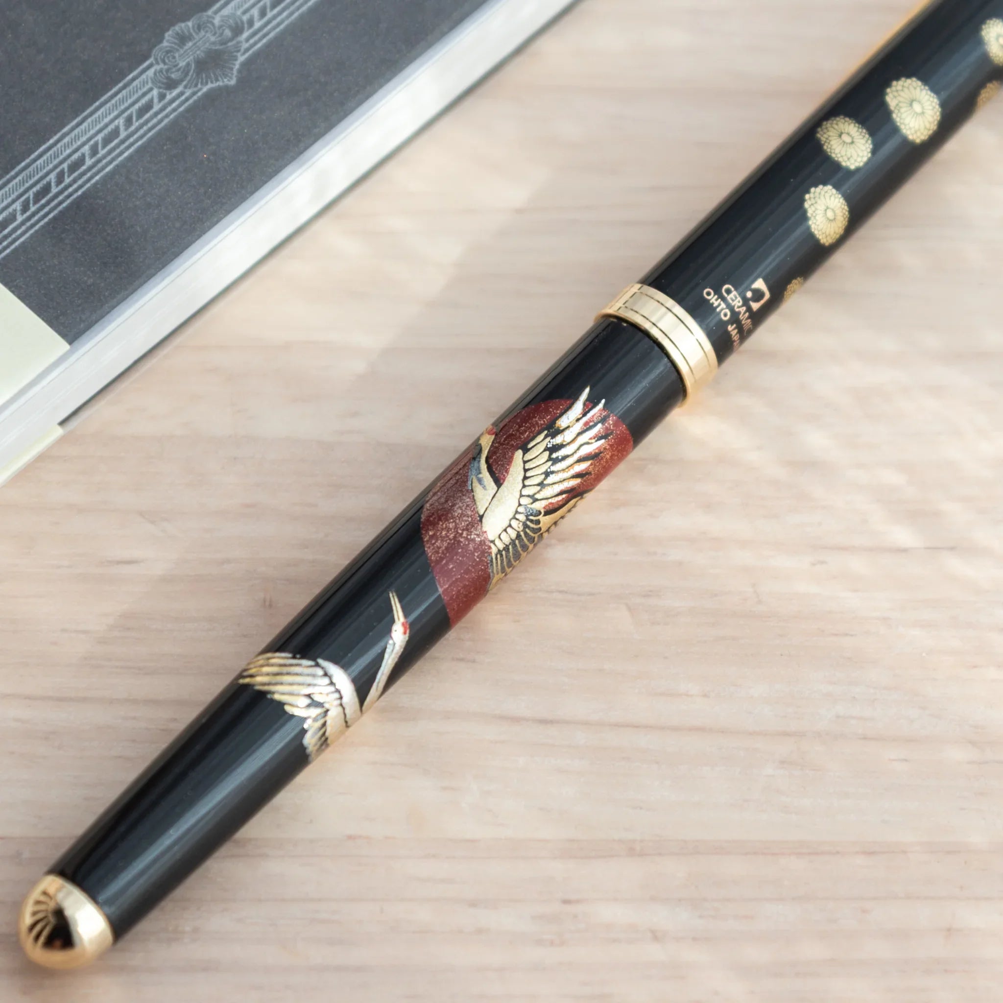 Close-up of Japanese ballpoint pen barrel showing two white cranes against red circular sun and gold chrysanthemum dots
