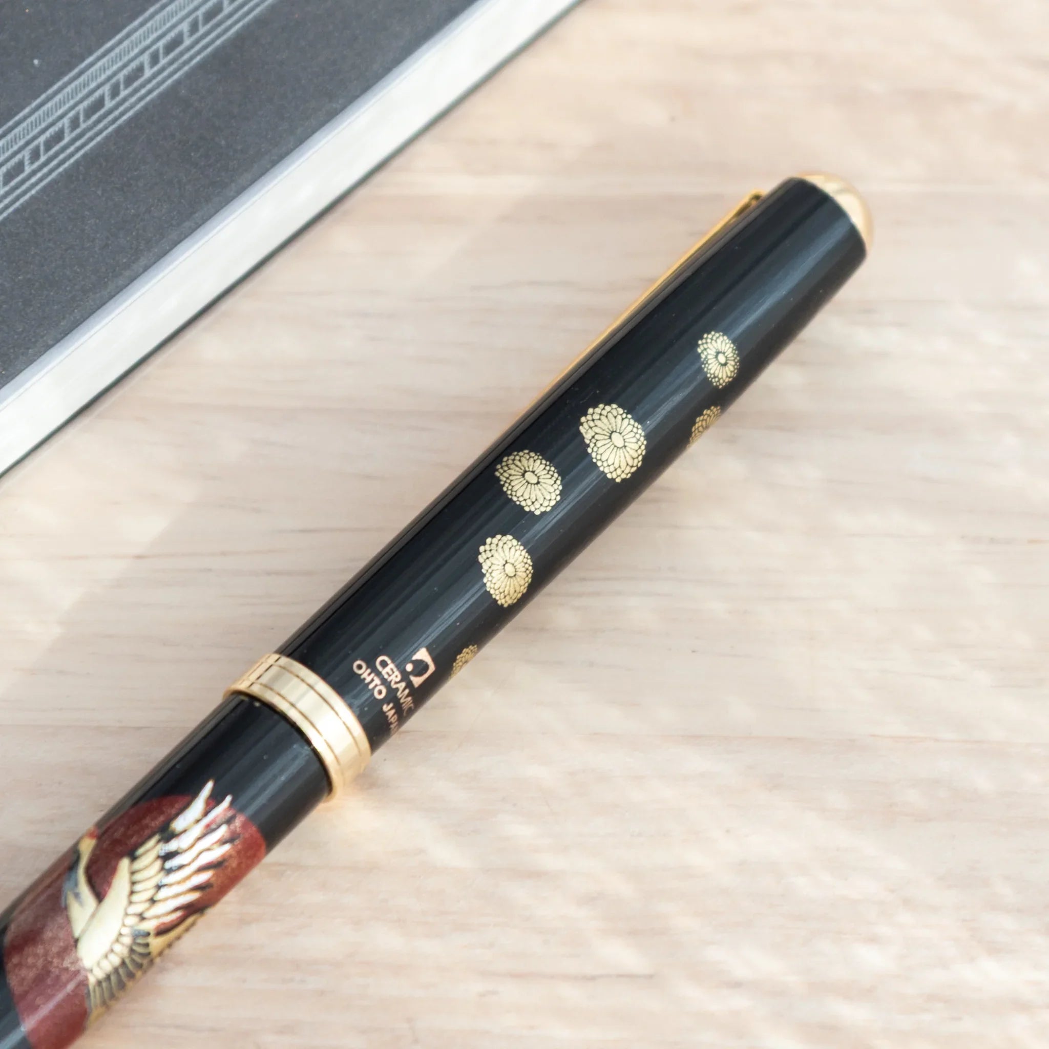 Close-up of Japanese ballpoint pen cap end showing gold chrysanthemum pattern on black barrel and Ceramic Ohto Japan label