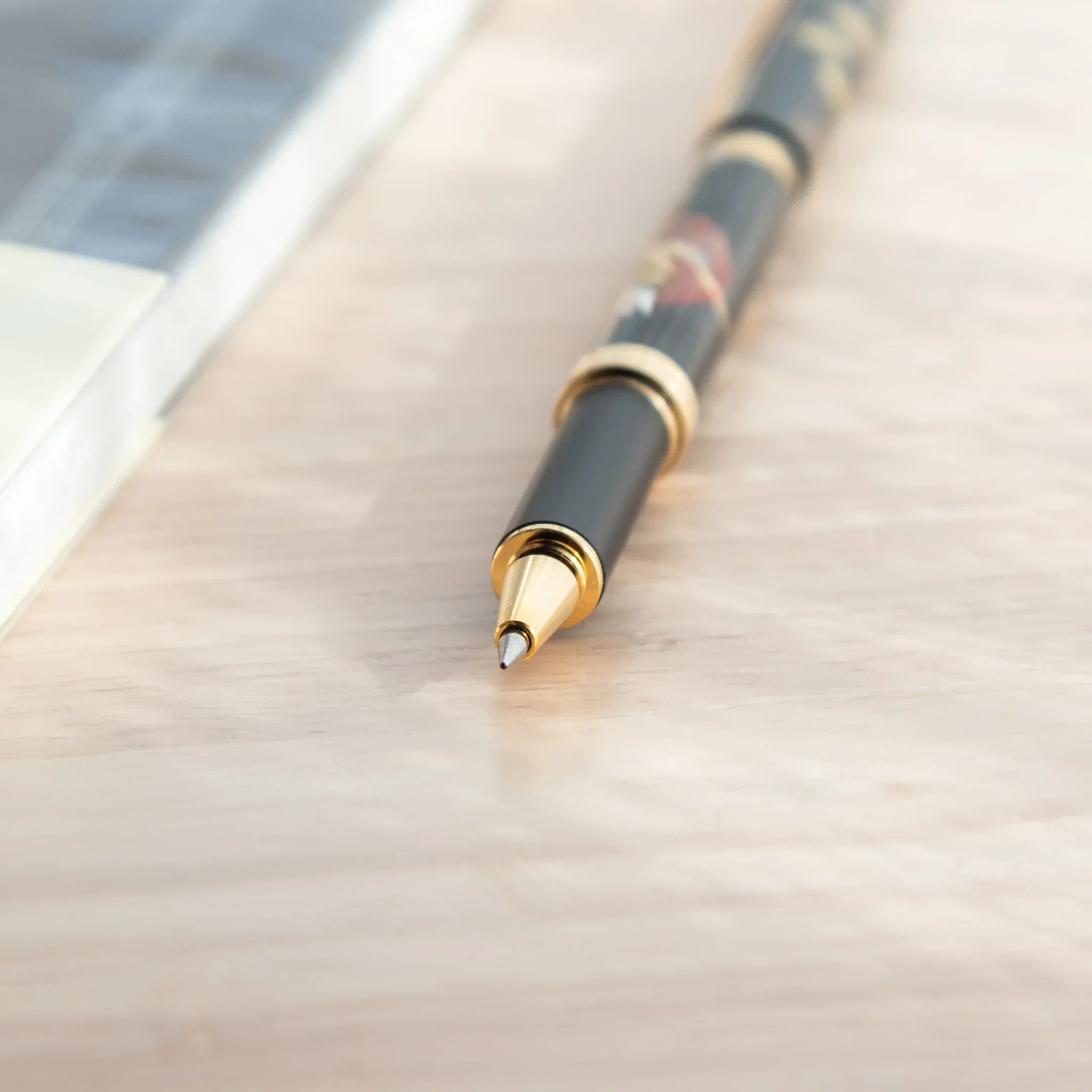 Macro close-up of Japanese ballpoint pen showing gold cone tip and metal ballpoint, with black barrel and gold ring visible