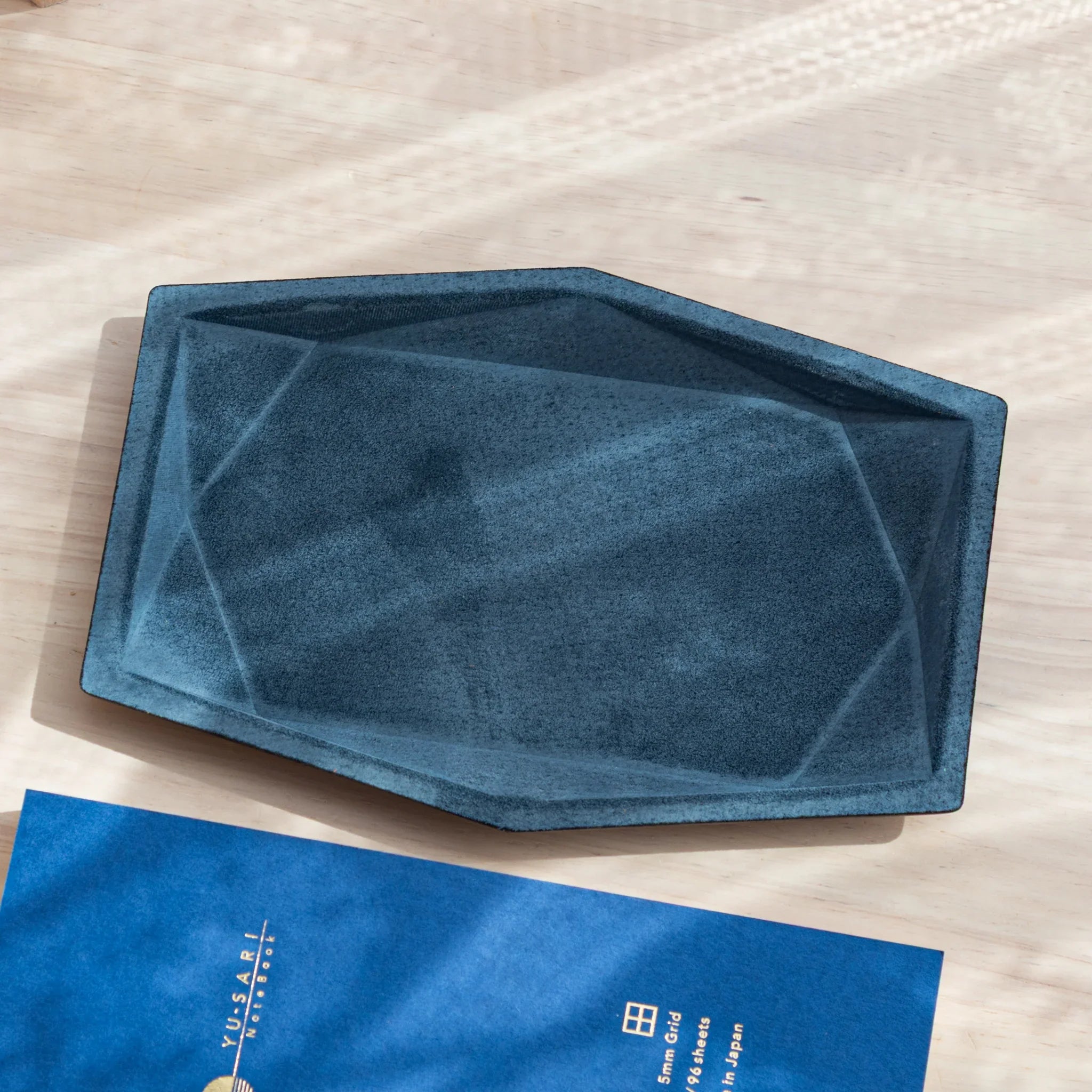Blue-gray suede wide hexagonal pen tray empty from an angle showing geometric faceted interior walls and black leather rim
