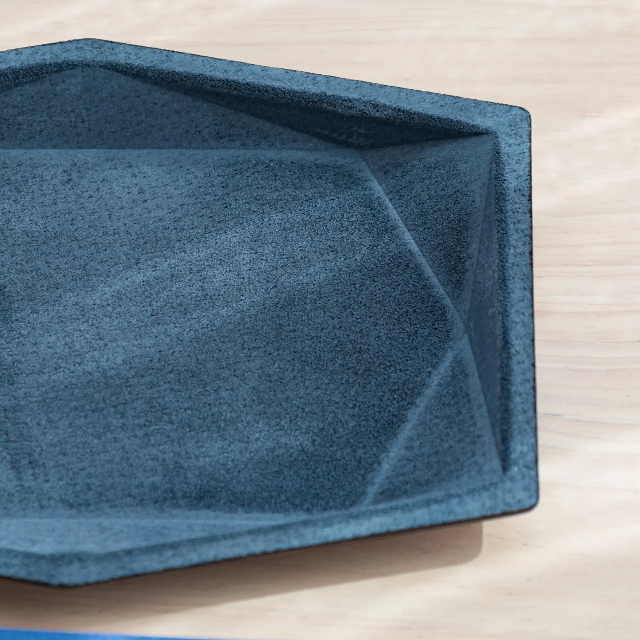 Close-up of blue-gray suede wide hexagonal pen tray interior corner showing geometric wall panels and black leather rim