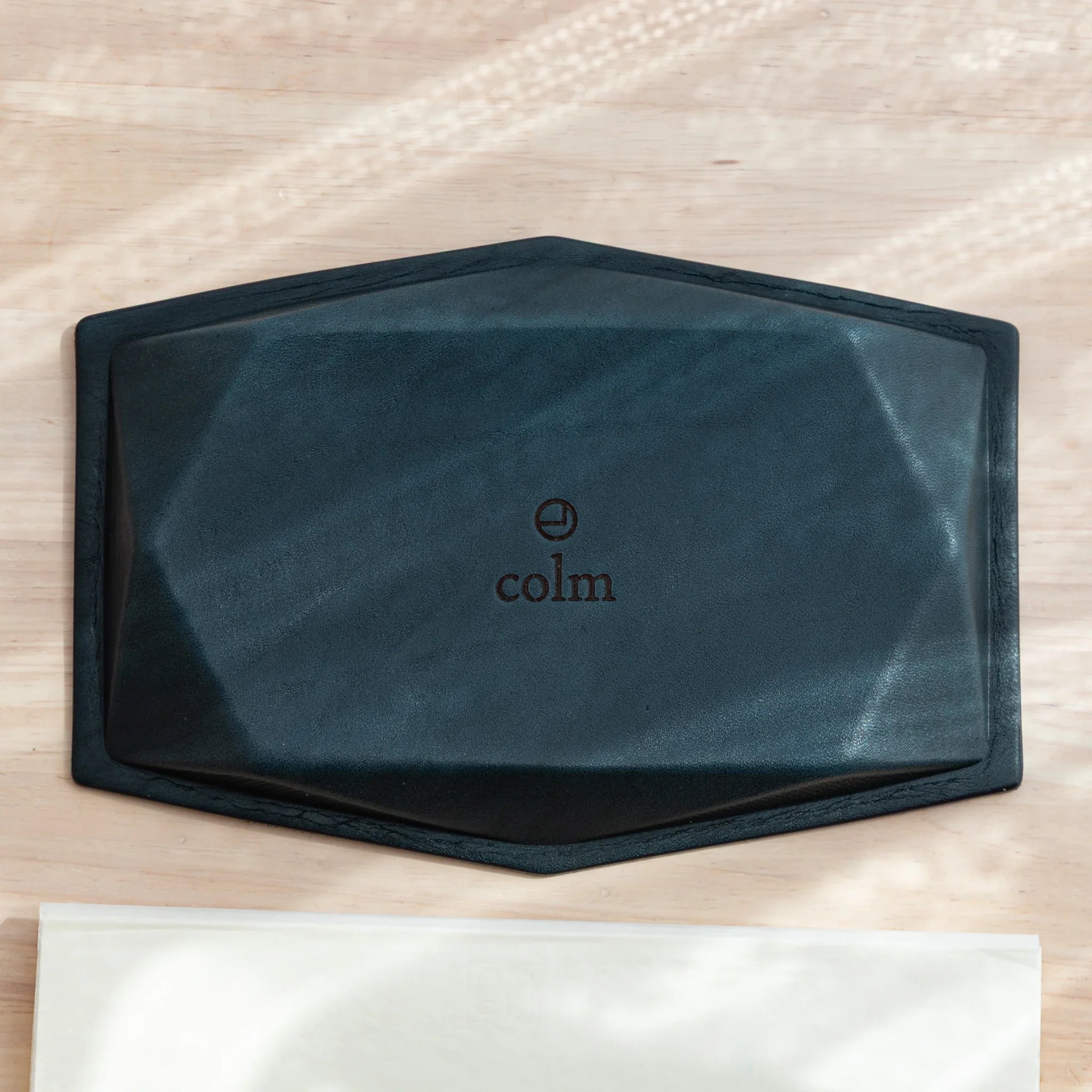 Overhead view of wide hexagonal pen tray upside down revealing full dark teal suede base with embossed colm logo