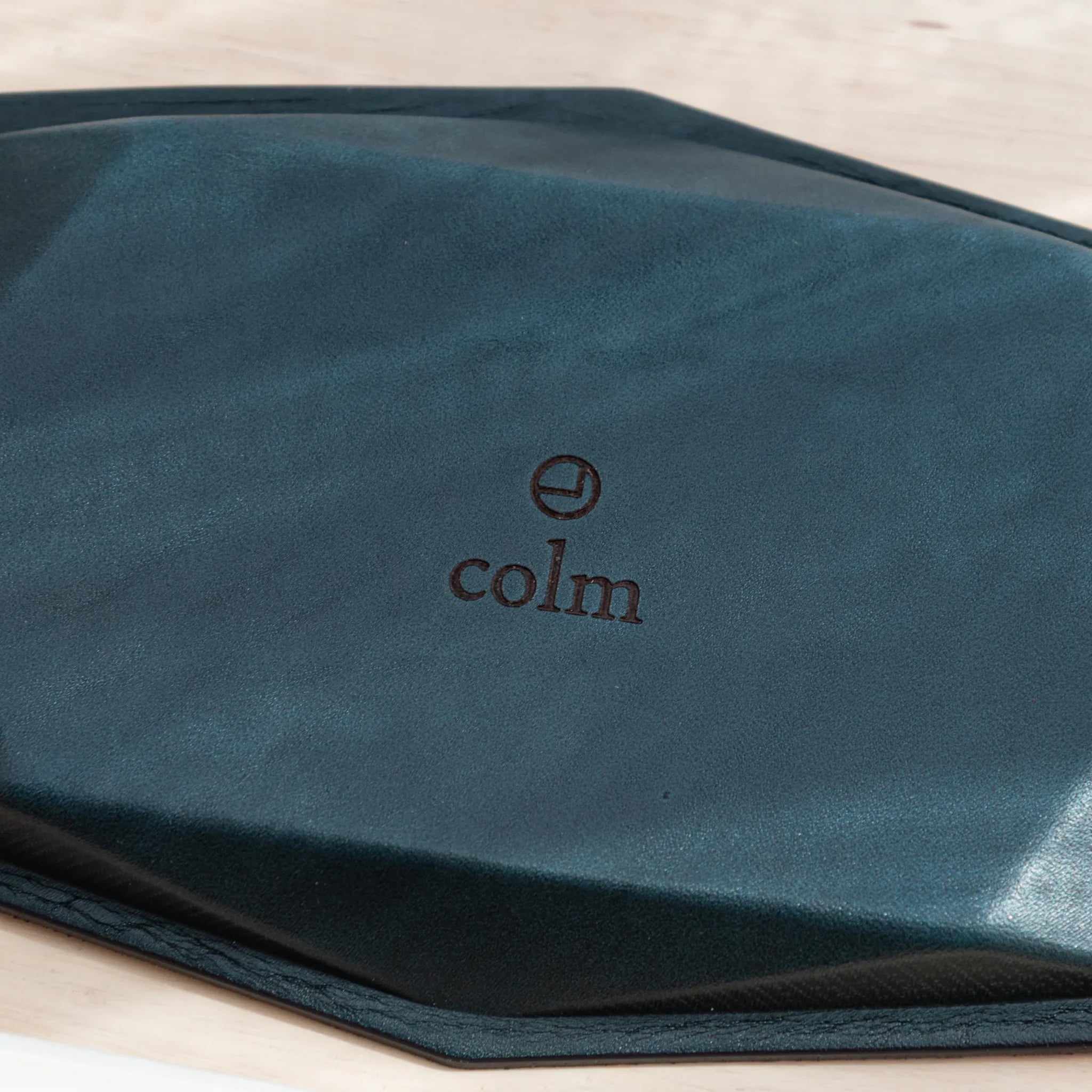Close-up of dark teal suede base of wide hexagonal pen tray with embossed colm logo showing suede texture and hex corner