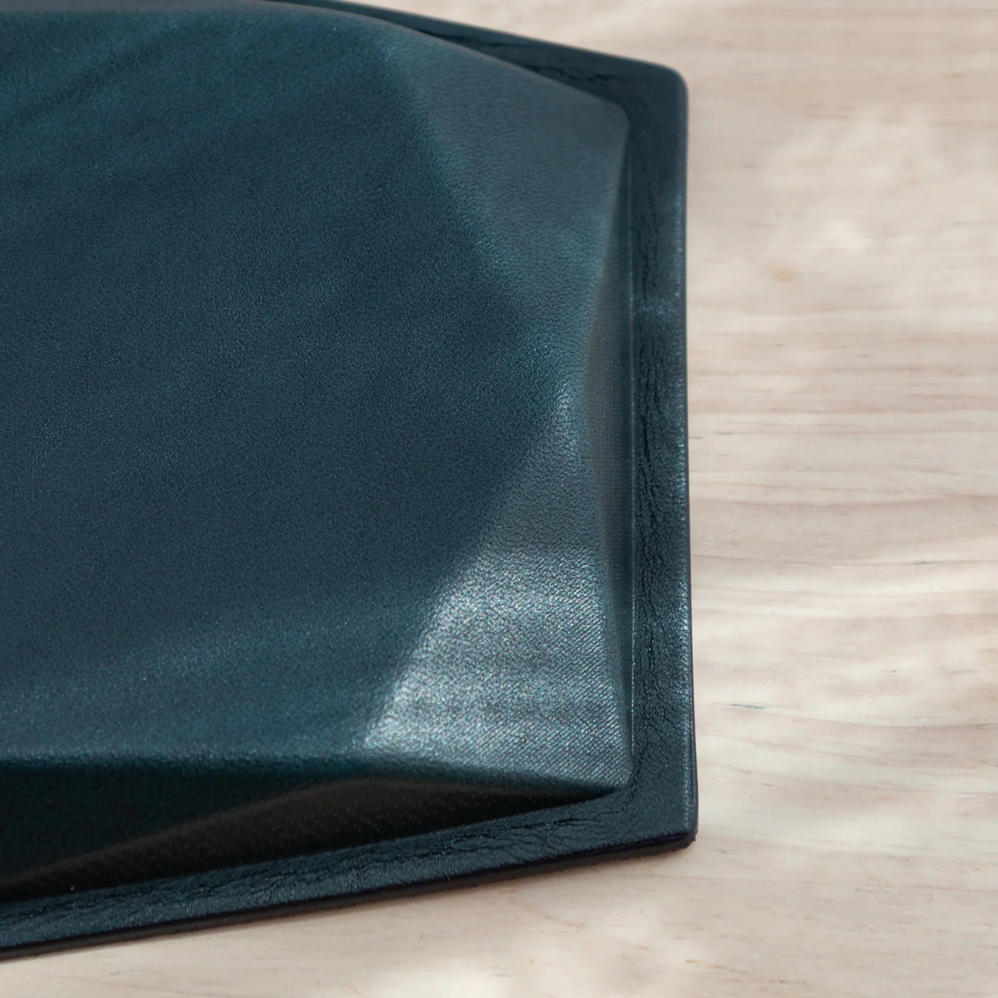 Corner detail of dark teal suede base showing suede texture and geometric angled corner with black leather edge