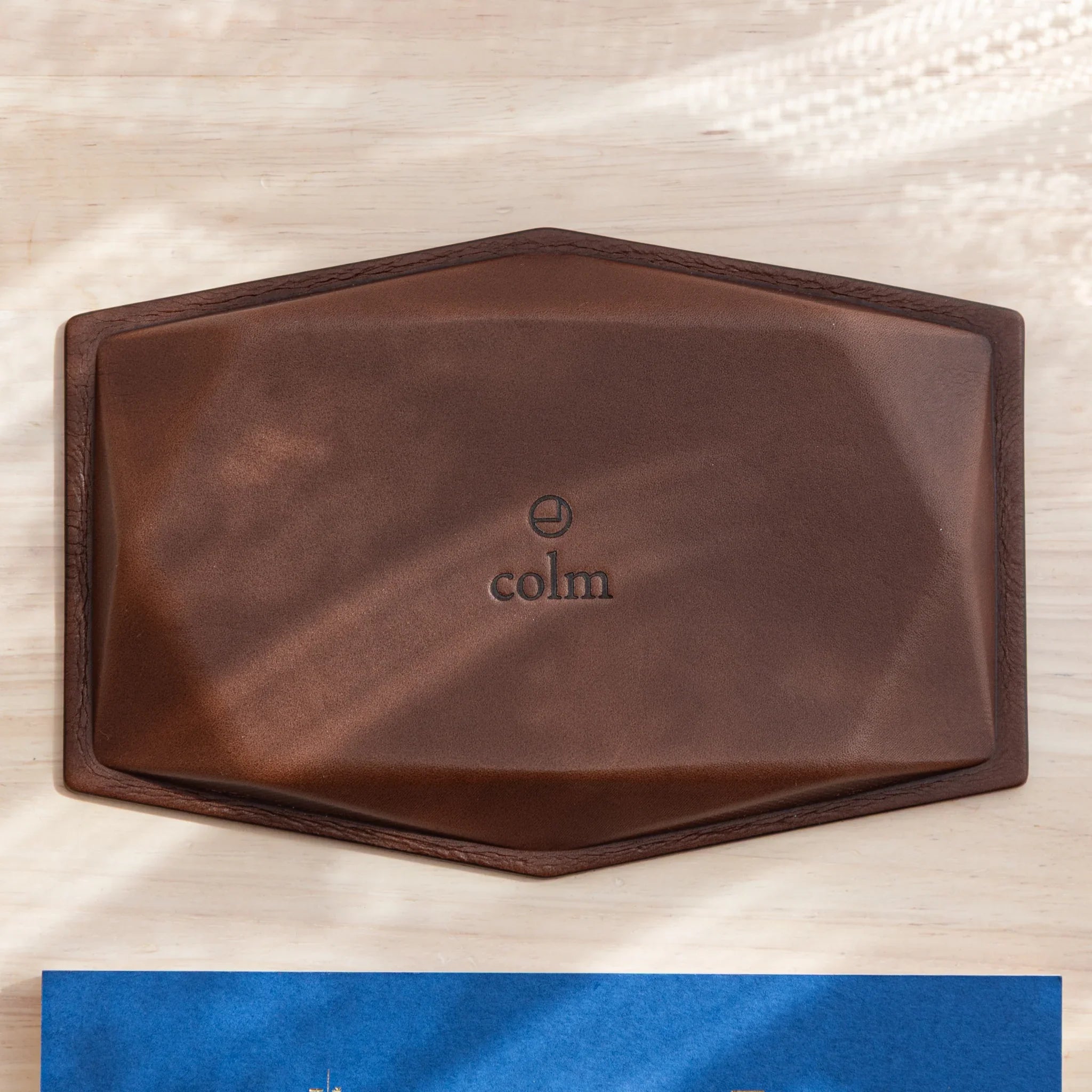 Overhead view of wide hexagonal pen tray upside down revealing full brown leather base with embossed colm logo