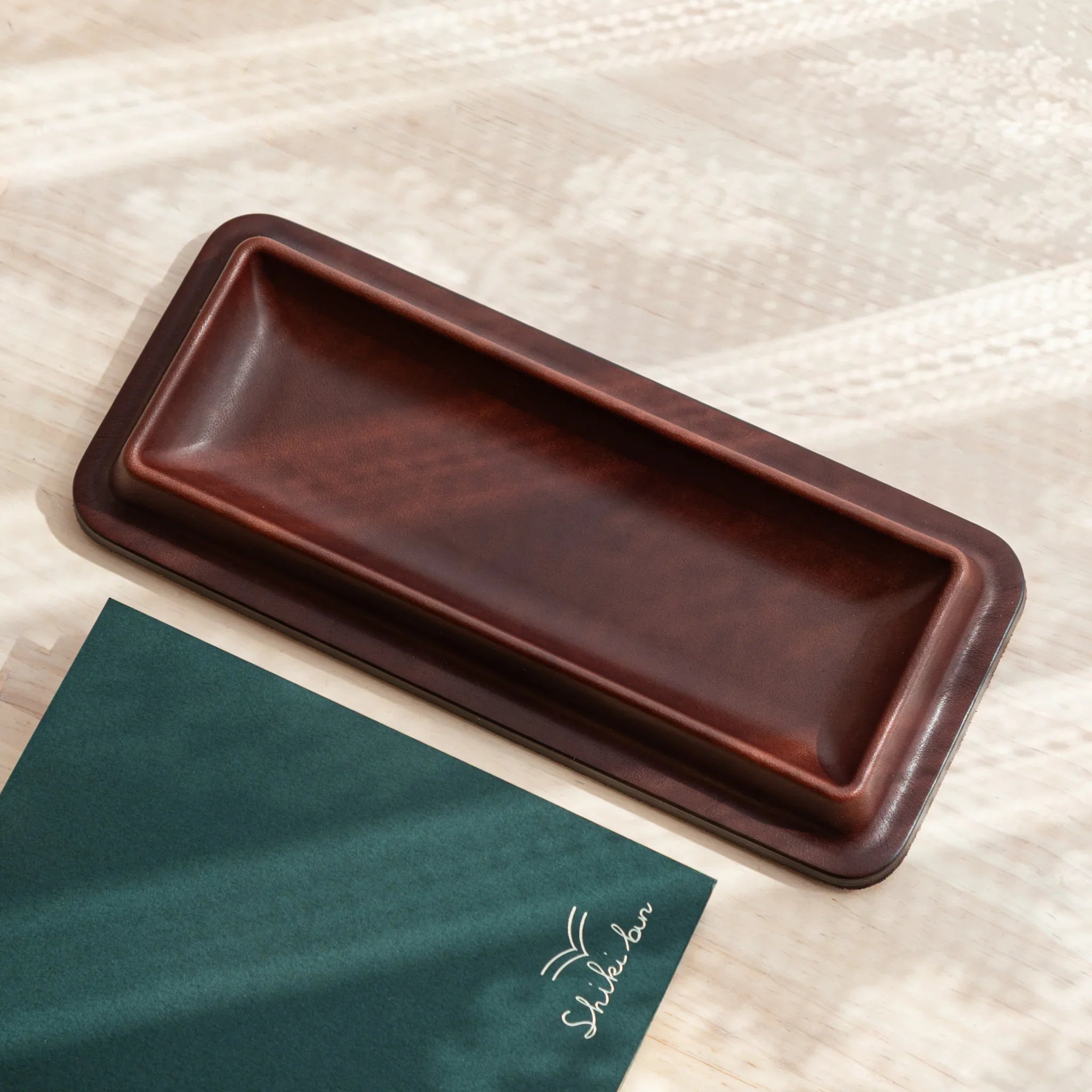 Empty burgundy leather pen tray displayed from top with green Shibui writing paper pad underneath tray