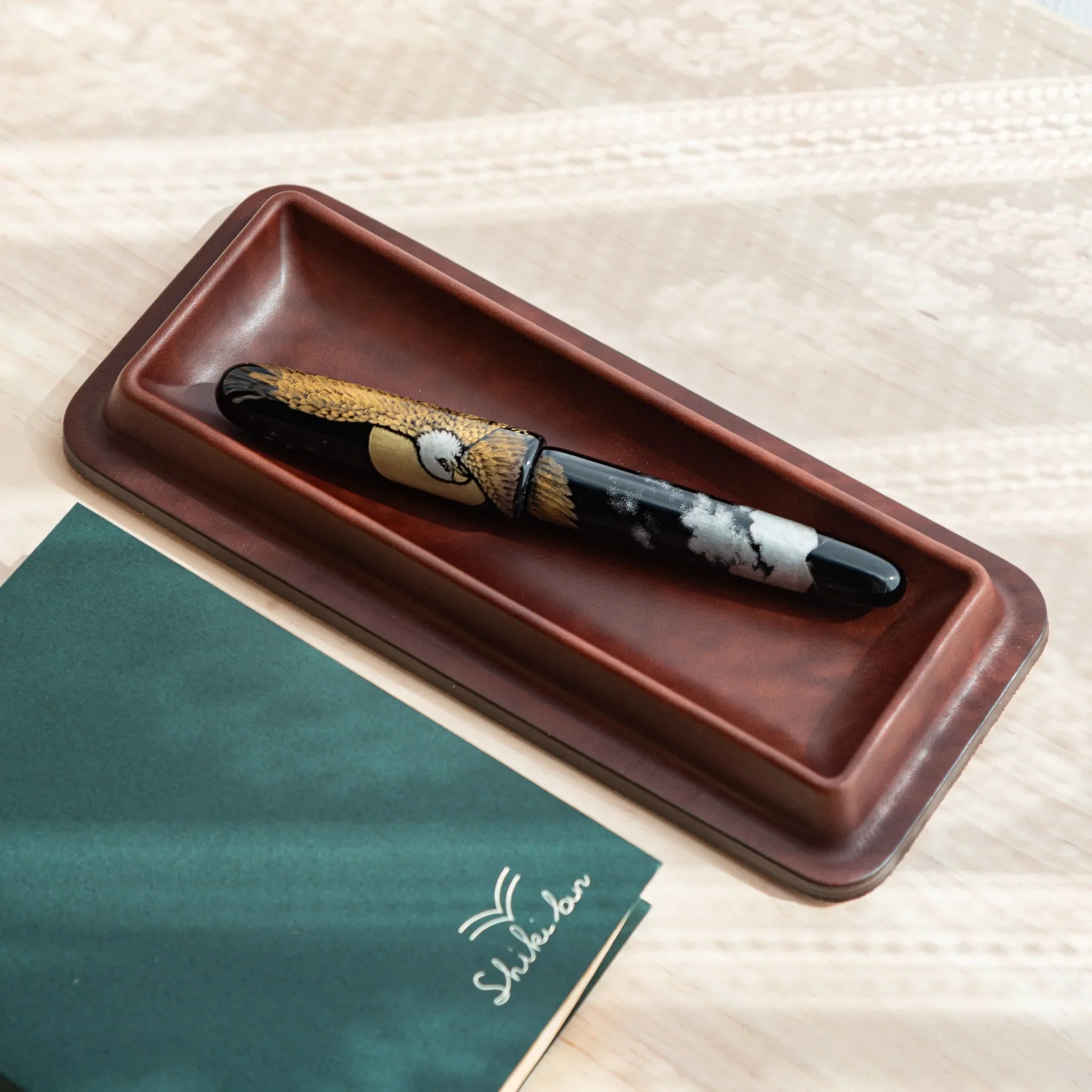 Burgundy leather pen tray angled view with brown and tan patterned decorative maki-e pen inside holder