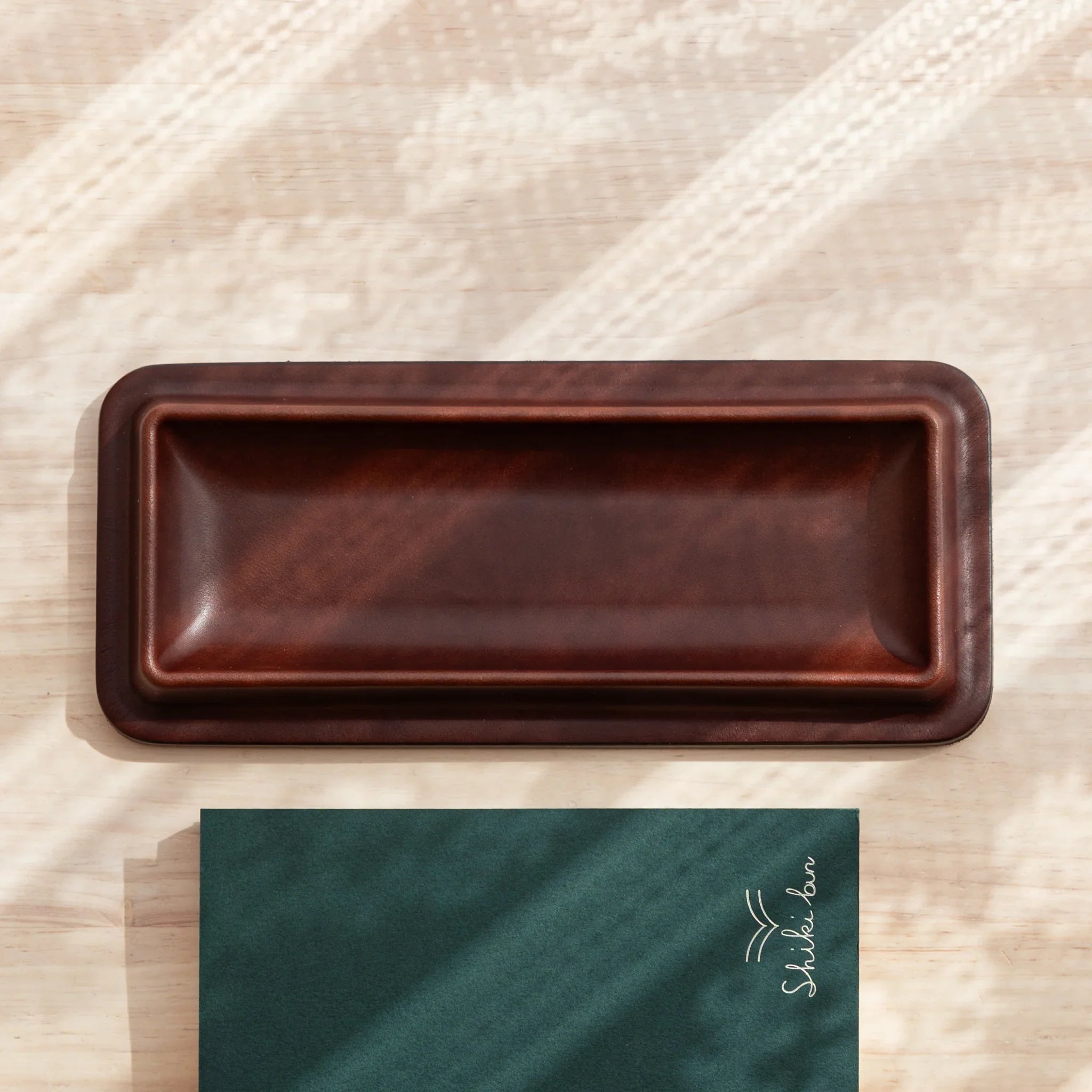 Burgundy leather pen tray empty overhead view positioned on light wooden surface with soft shadows shown