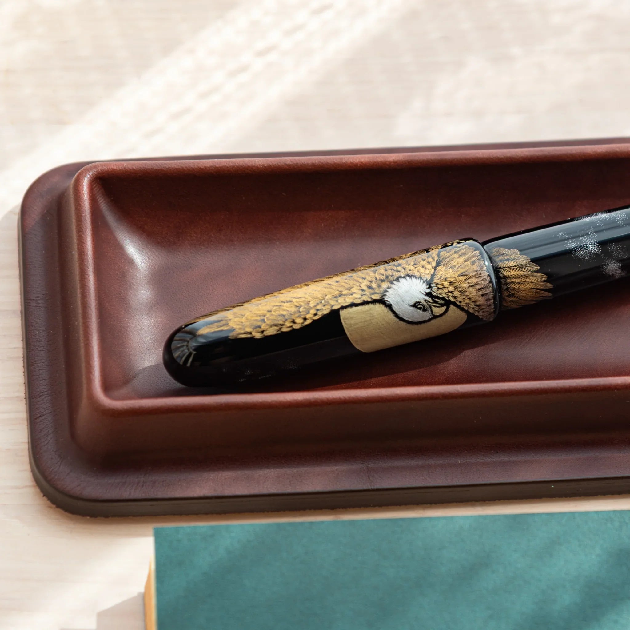 Burgundy leather pen tray angled showing brown patterned maki-e pen with decorative detail work visible