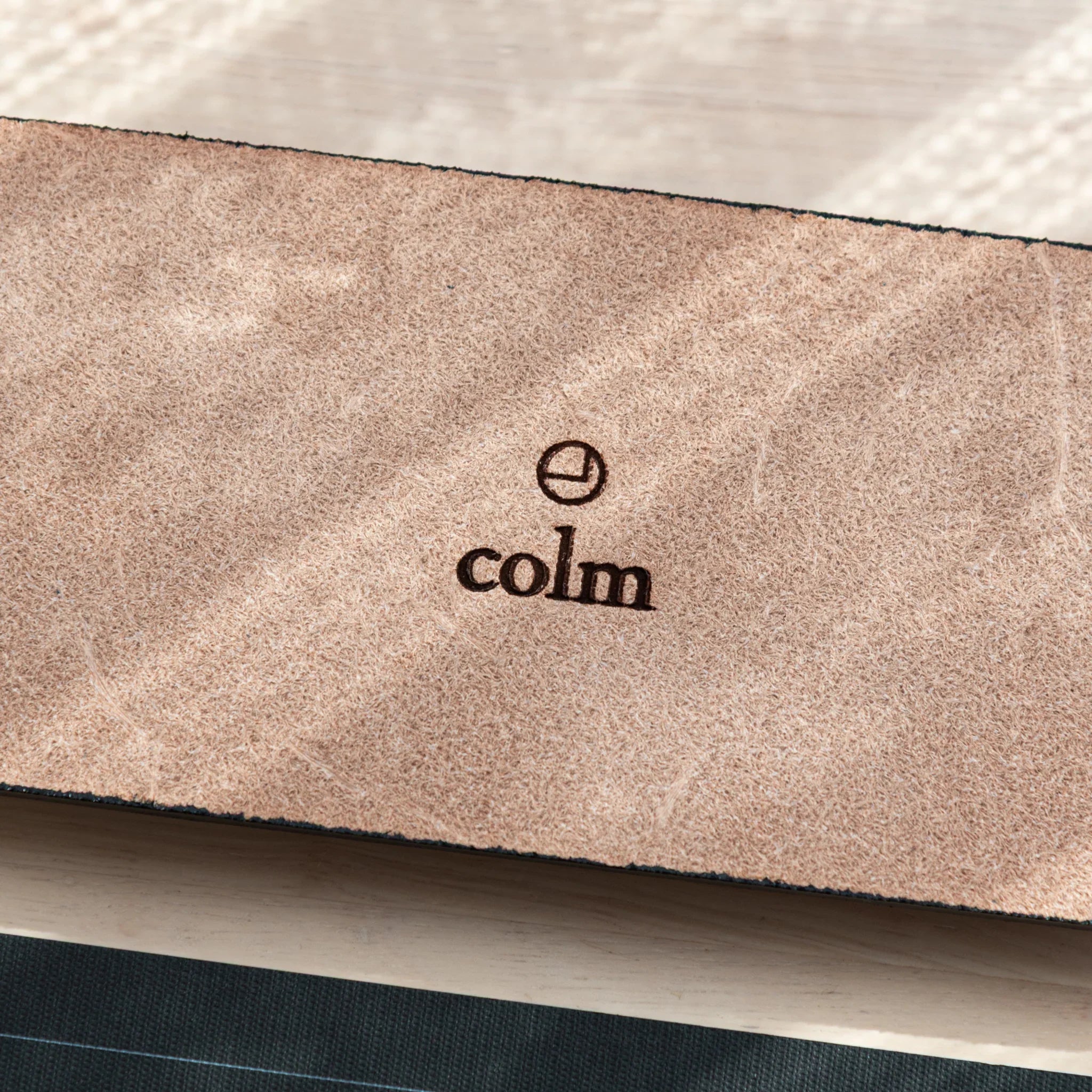 Black suede pen tray back with colm brand mark imprint visible on material backing surface shown clearly