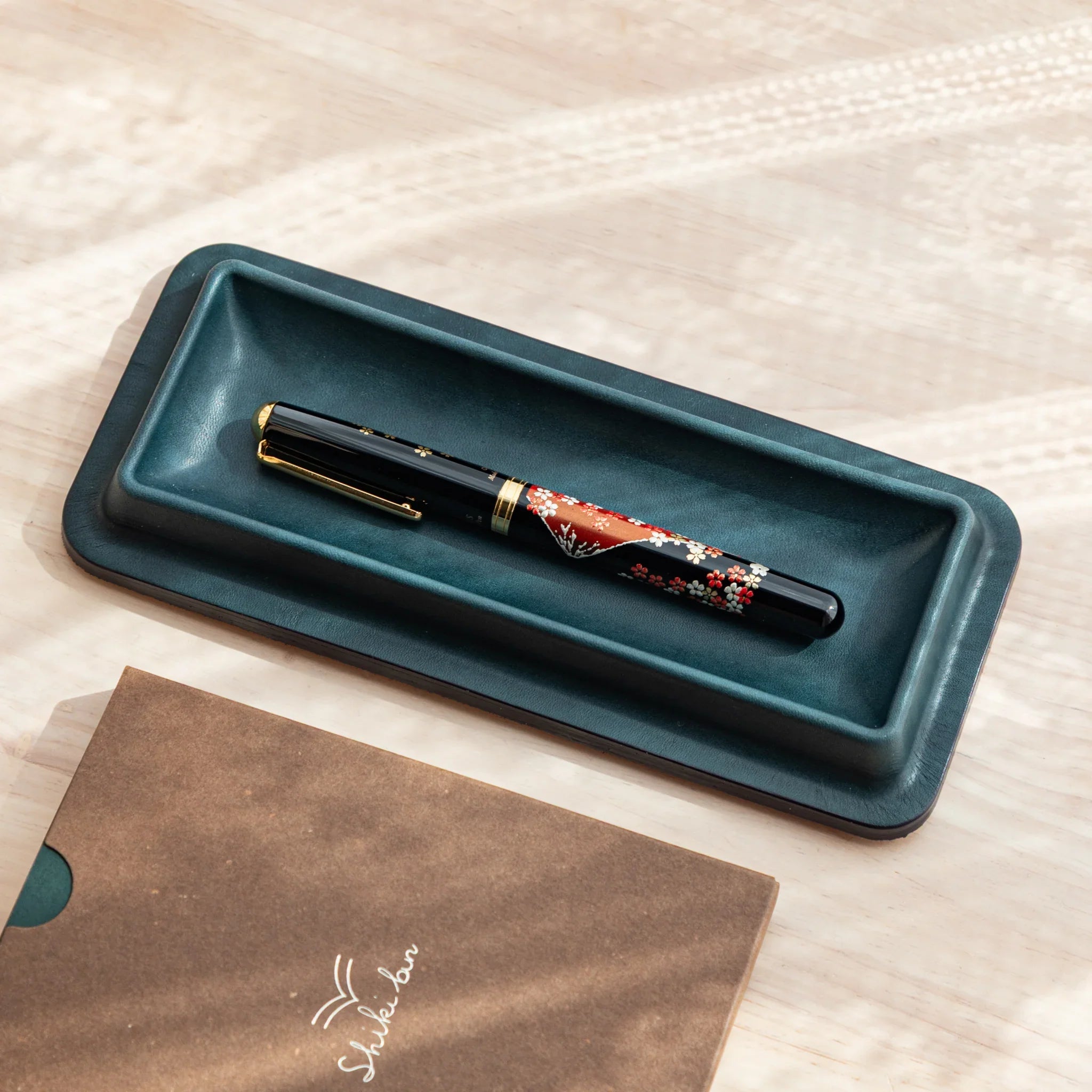 Olive green leather pen tray overhead with red burgundy decorative maki-e pen placed inside the tray