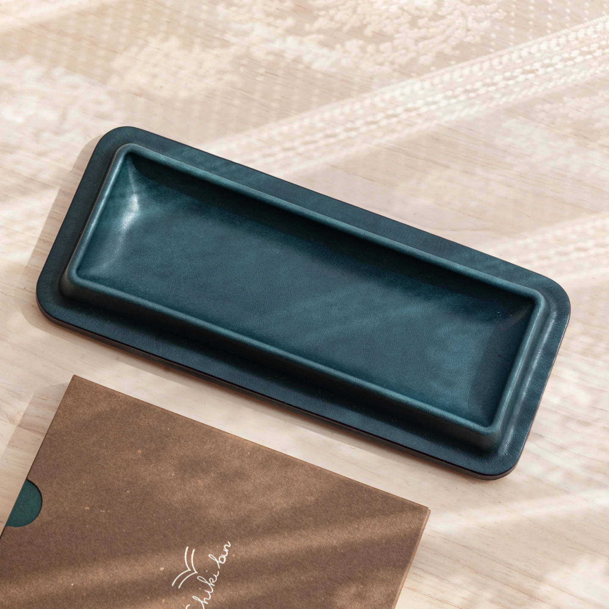 Olive green leather pen tray empty view from above on wooden background with natural lighting visible