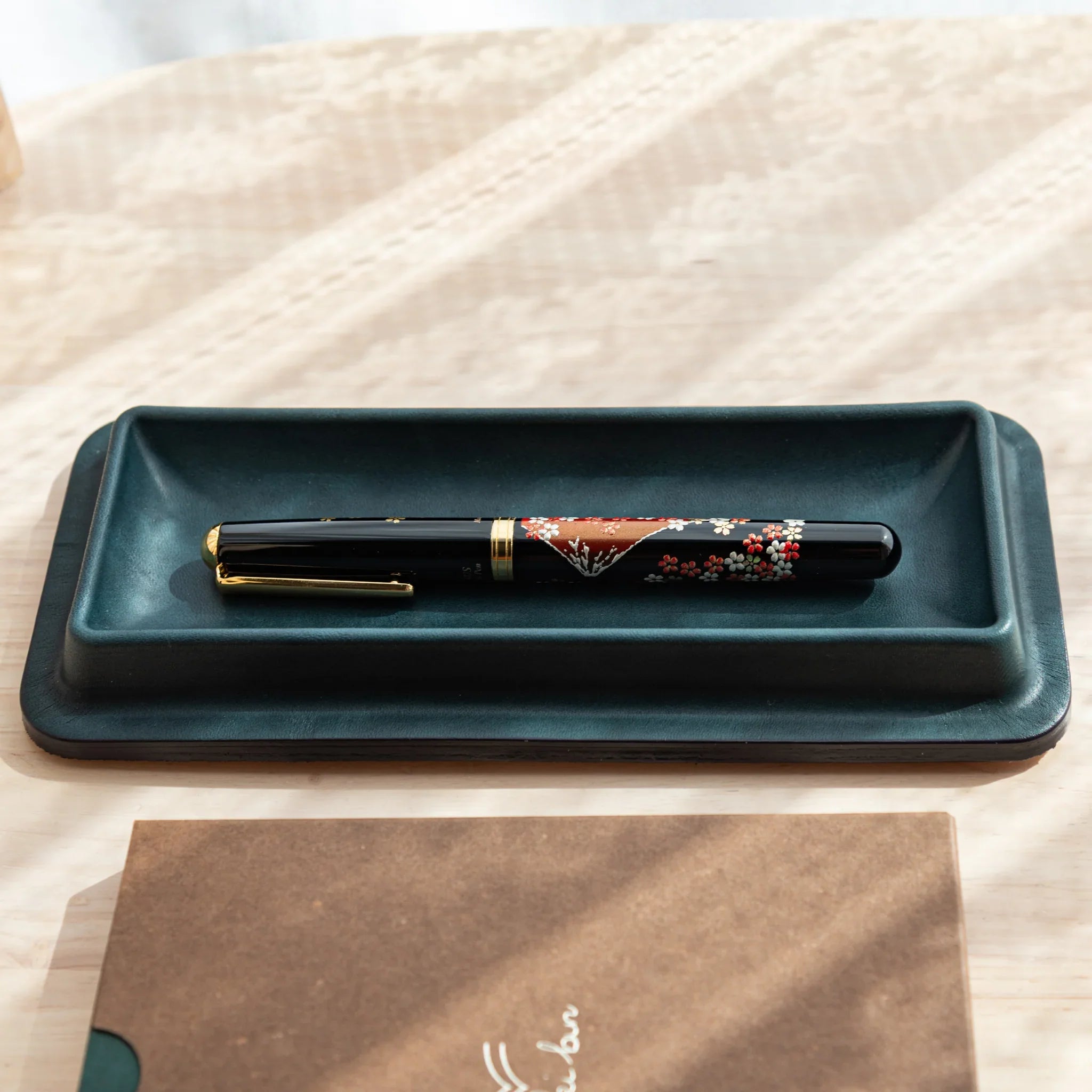 Olive green leather pen tray angled view displaying decorated maki-e pen with red flower pattern design