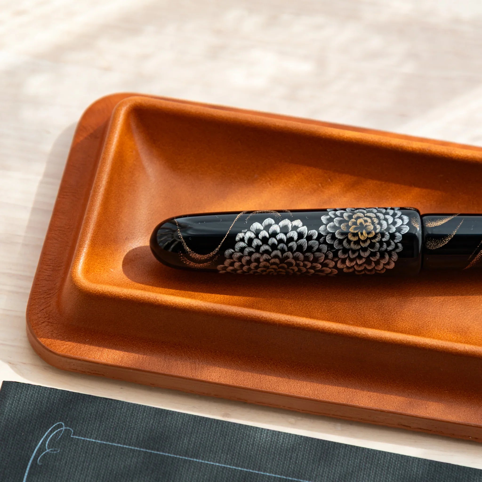 Cognac leather pen tray side profile showing black decorative maki-e pen positioned inside storage slot