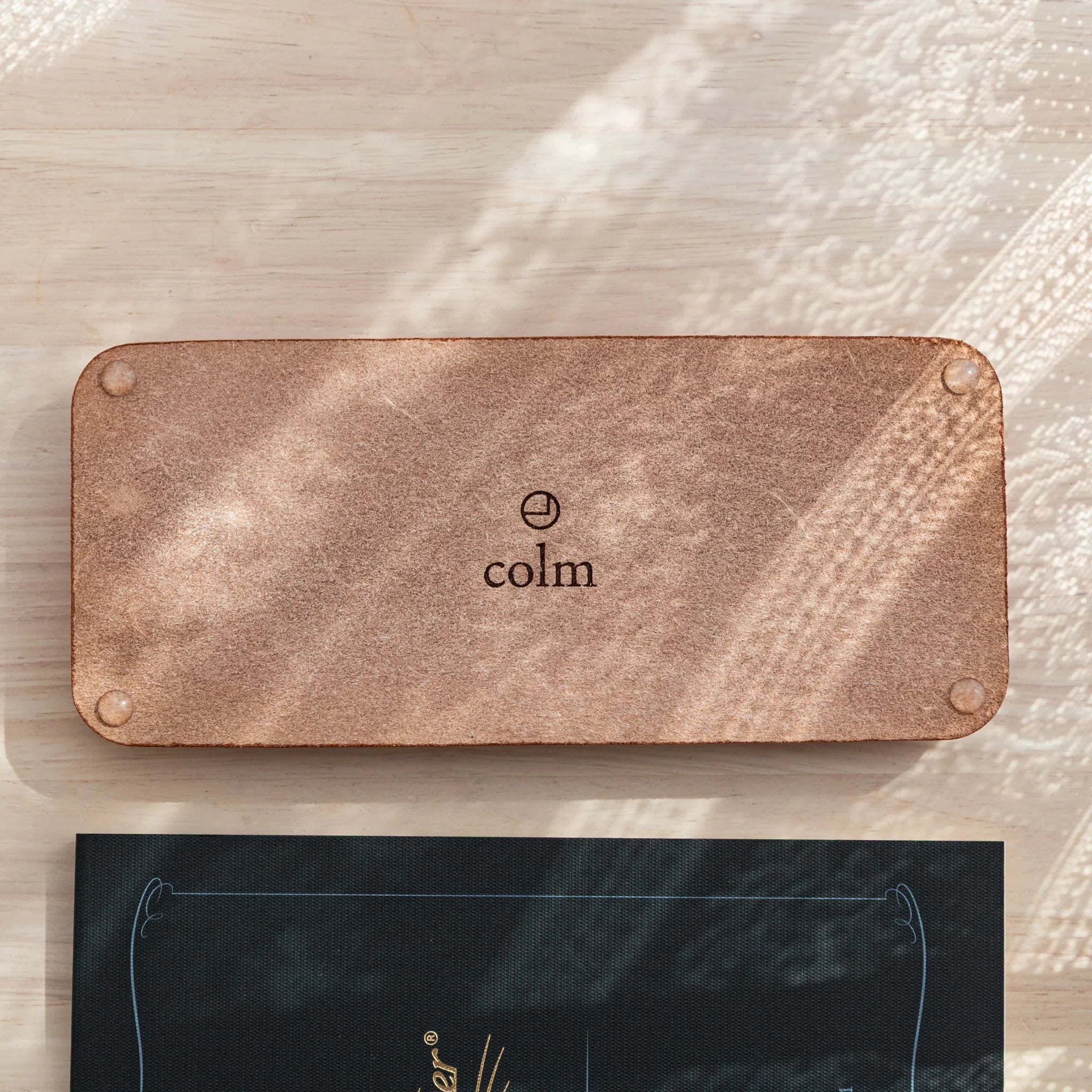 Tan colored suede pen tray underside featuring colm logo embossed on the backing surface of the tray