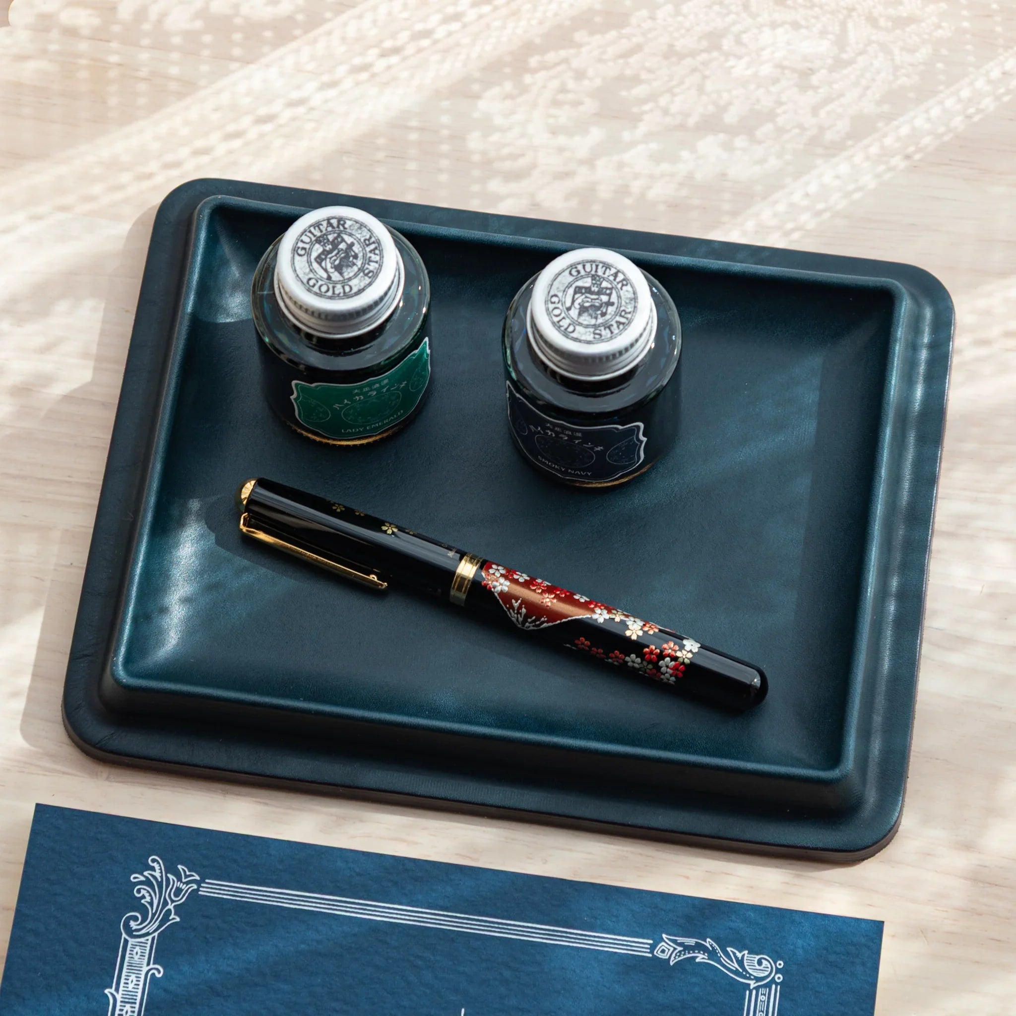 Teal wide rectangular leather pen tray viewed directly from above, displaying three fountain pens and glass ink bottle