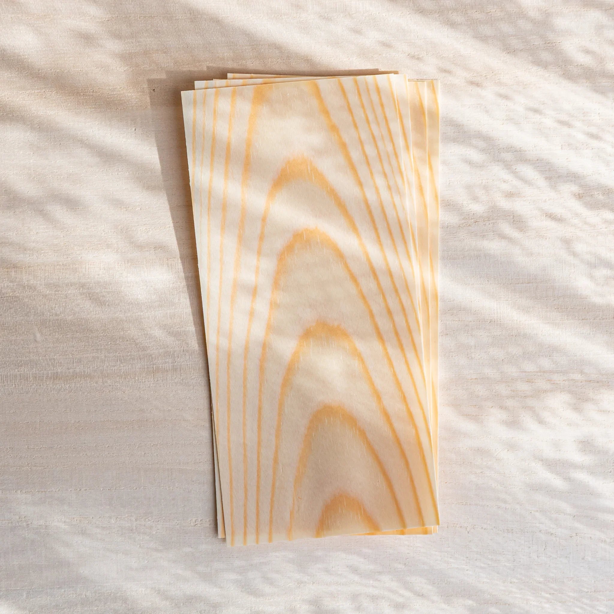 Thin wood message cards stacked on a light desk, with soft curtain shadows highlighting the natural pine grain