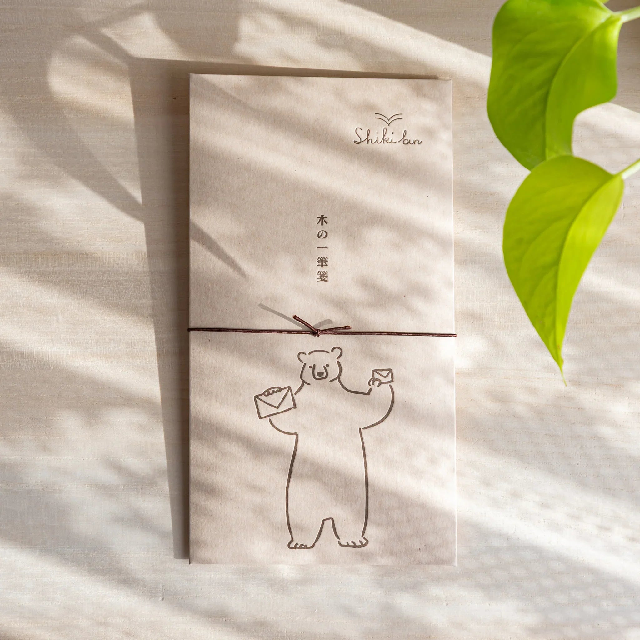 Thin wood message card with bear illustration placed on a light desk, with soft shadows and a green leaf in frame