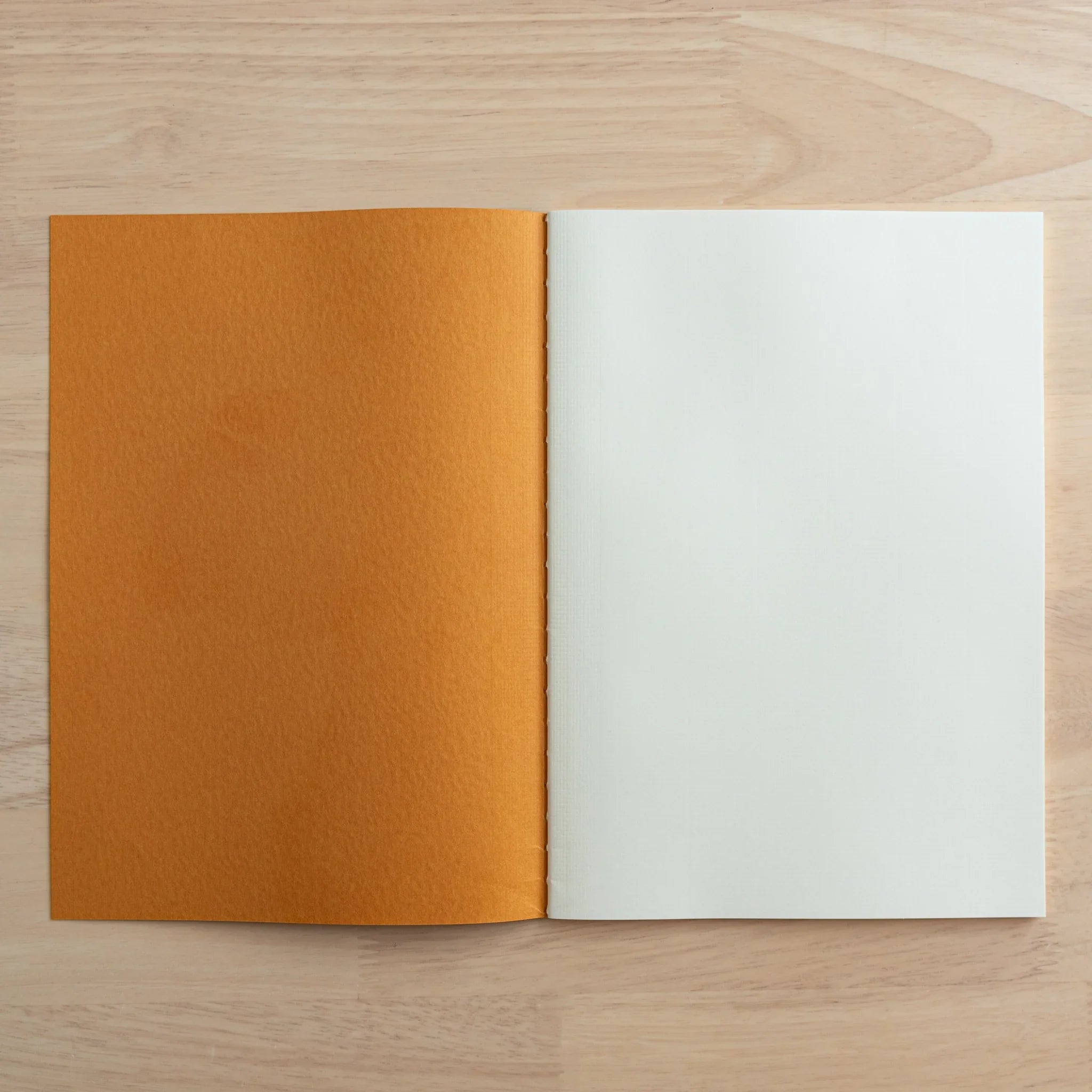 Tsubame Fools Cream Notebook open flat displaying grid-patterned cream interior pages and thread-sewn binding detail