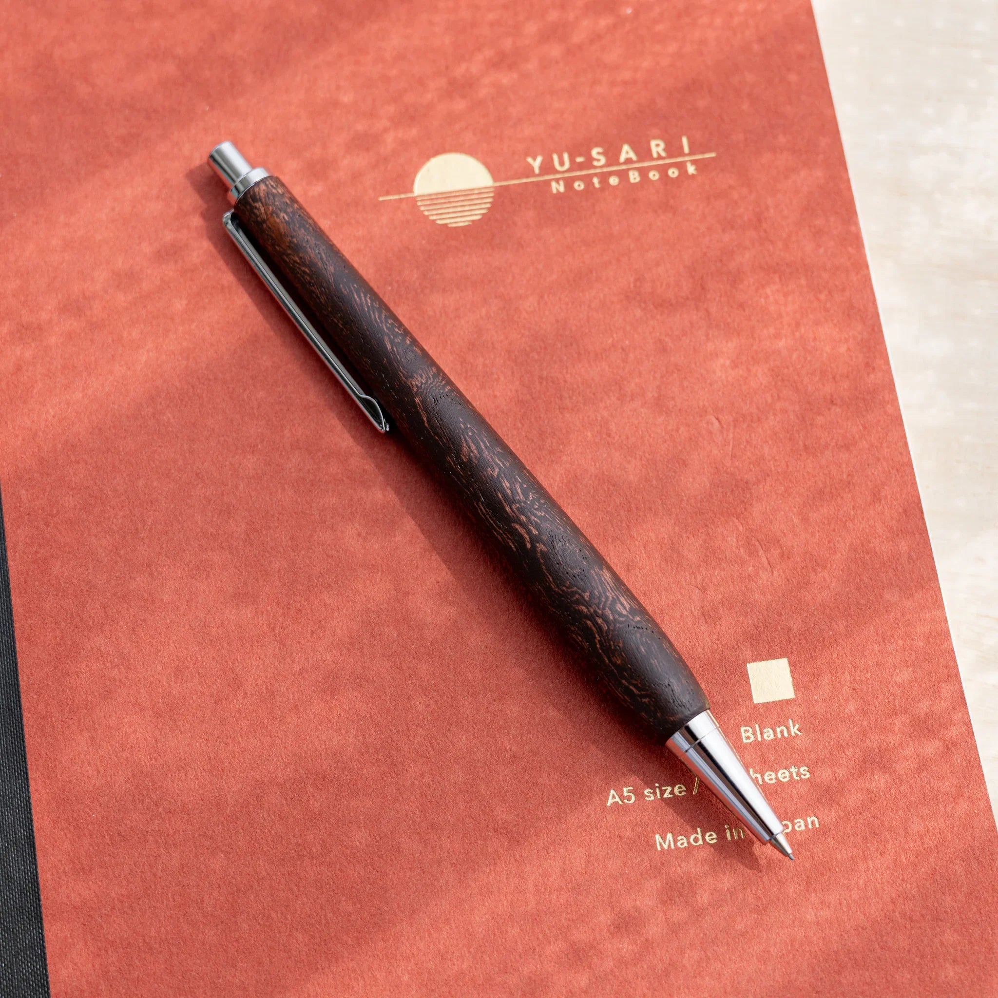 Zelkova wood urushi lacquered mechanical pencil in dark reddish-brown, Japanese keyaki, full body on red surface