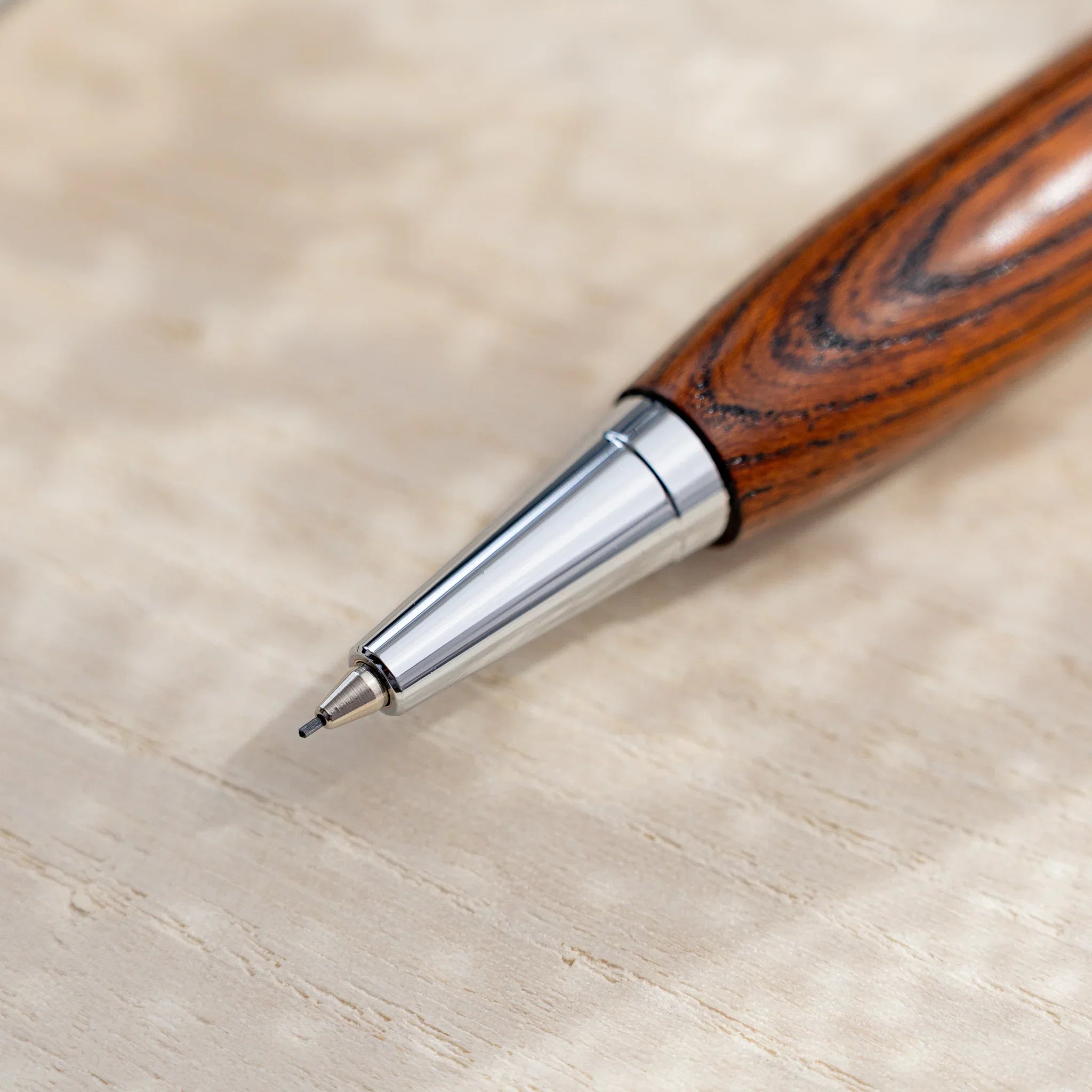 Amber-brown zelkova wood urushi mechanical pencil, close-up of silver cone tip and pencil lead, Japanese keyaki